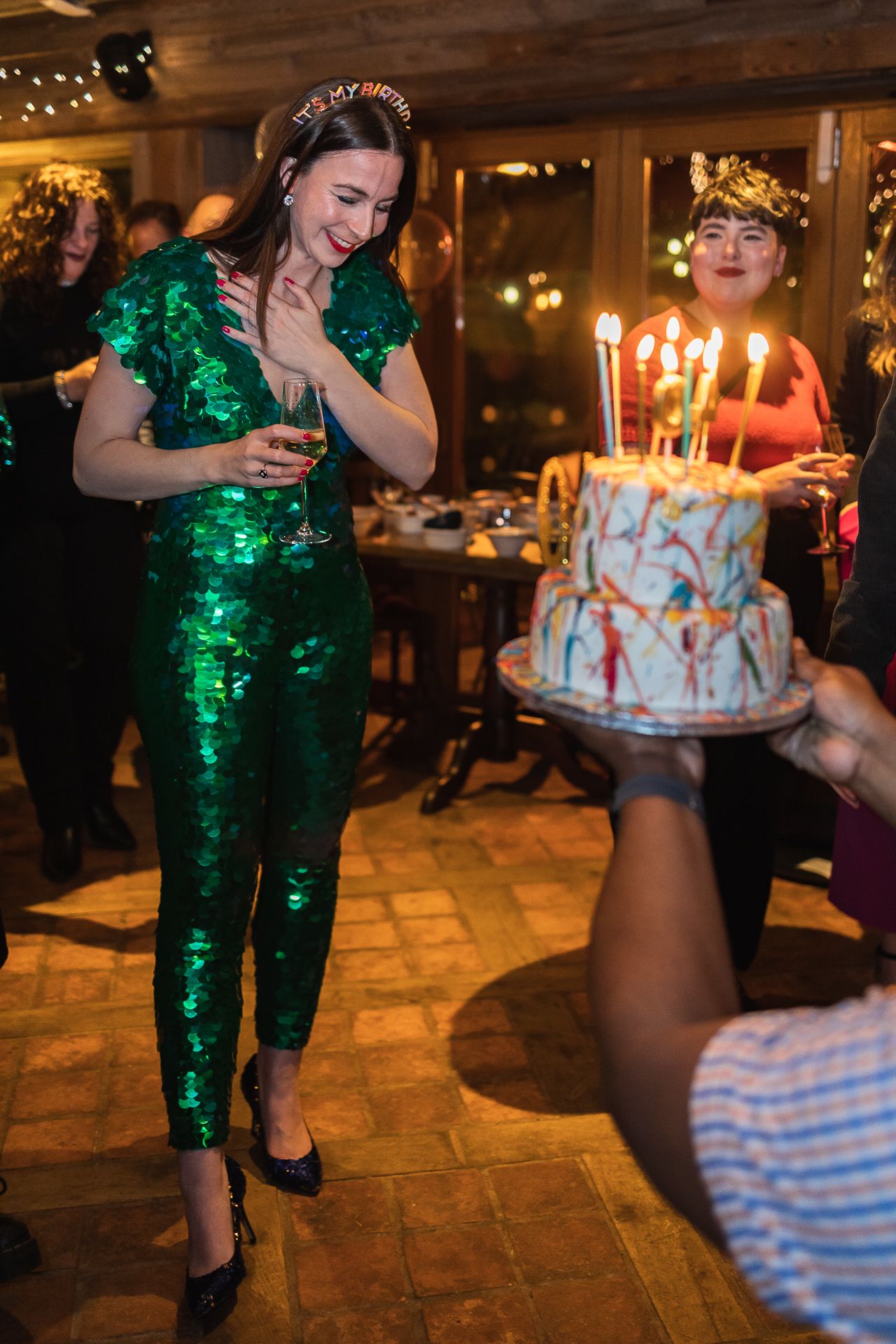 Birthday girl in a fabulous green sequin jumpsuit blows out the candles on her birthday cake in pub in Richmond, London.