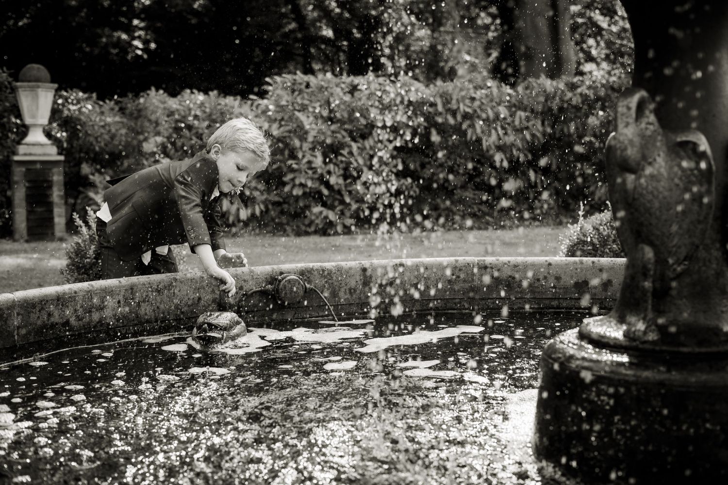 Young boy playing at the water fountain at summer wedding reception.