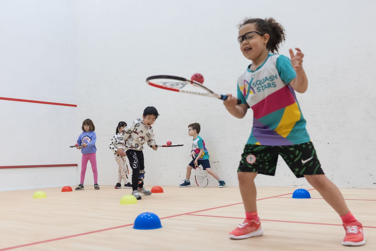 In action shot of junior squash class at Oakleigh Park tennis and squash club. Young girl is balancing ball on her racket and walking.