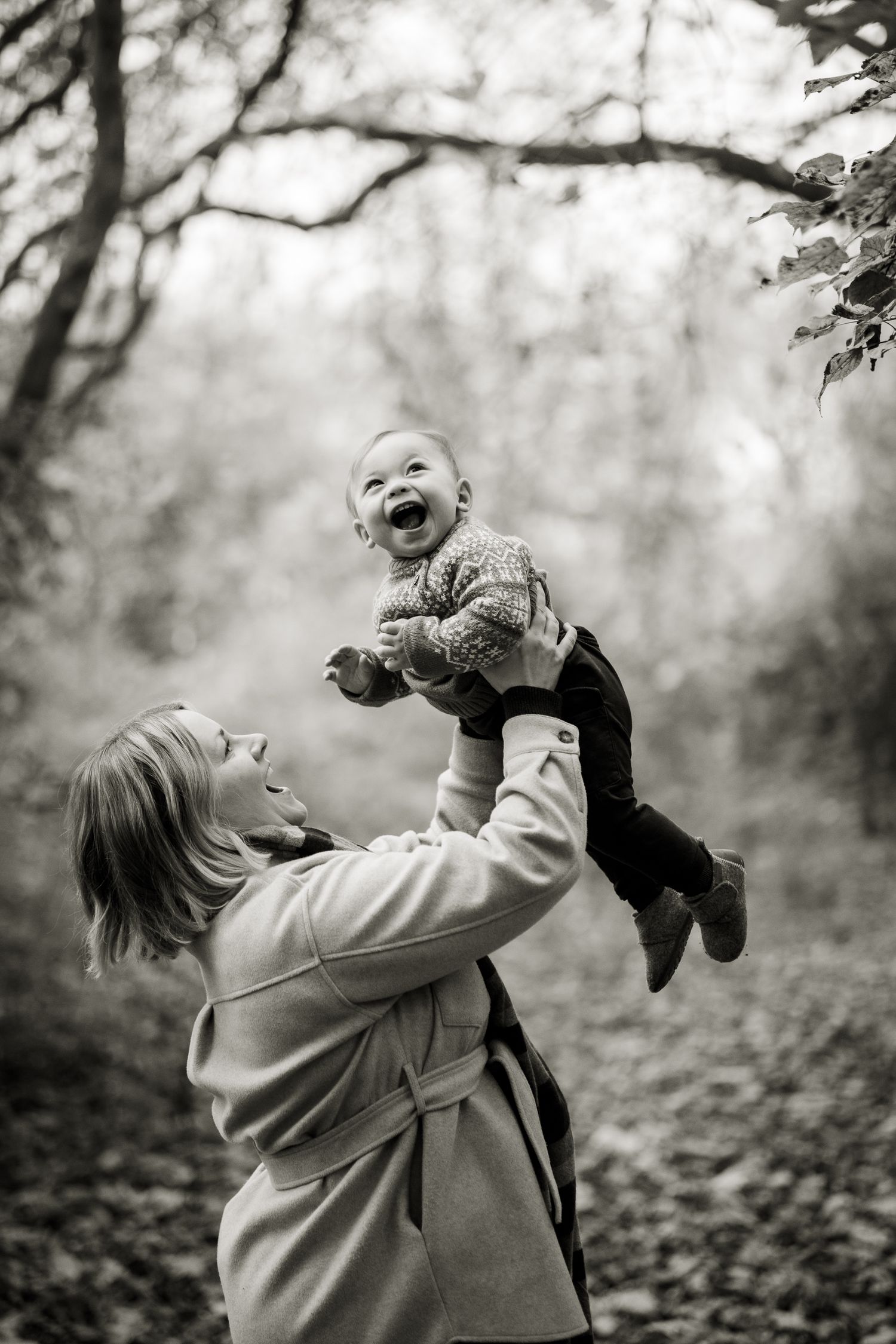 Black and white image of a mum throwing her toddler into the air and the huge grin on his face.