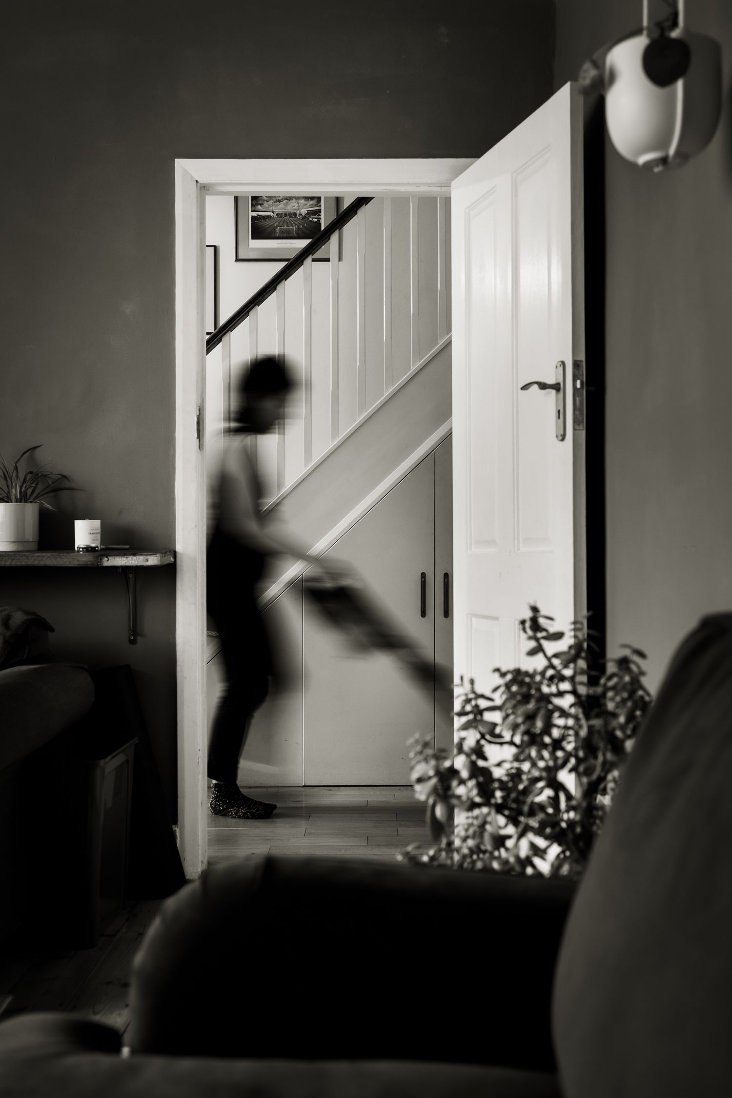 Photo through the doorway showing a (blurry) person hoovering. Blur to indicate movement.
