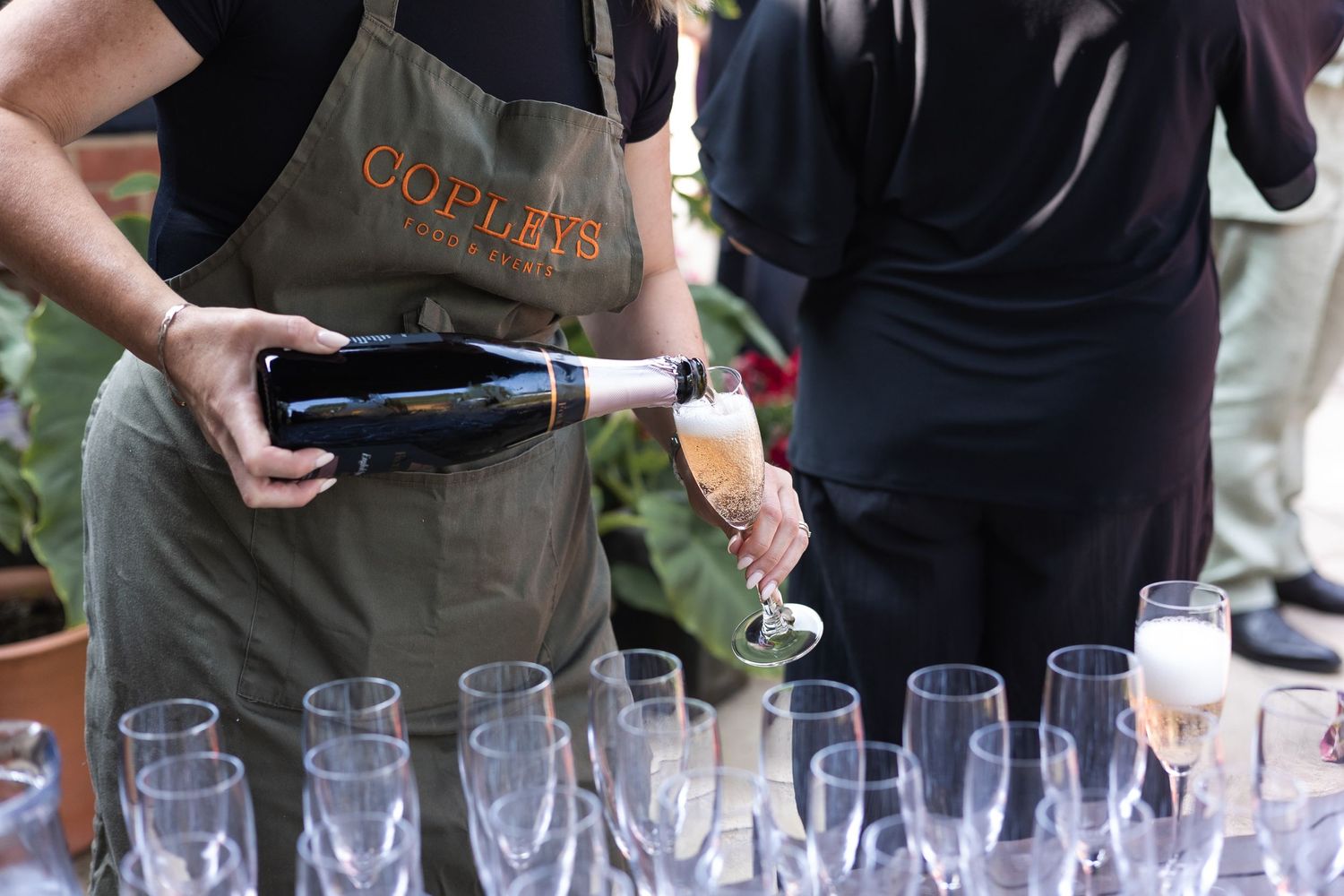 The wedding suppliers pouring champagne into the glasses for the guests.