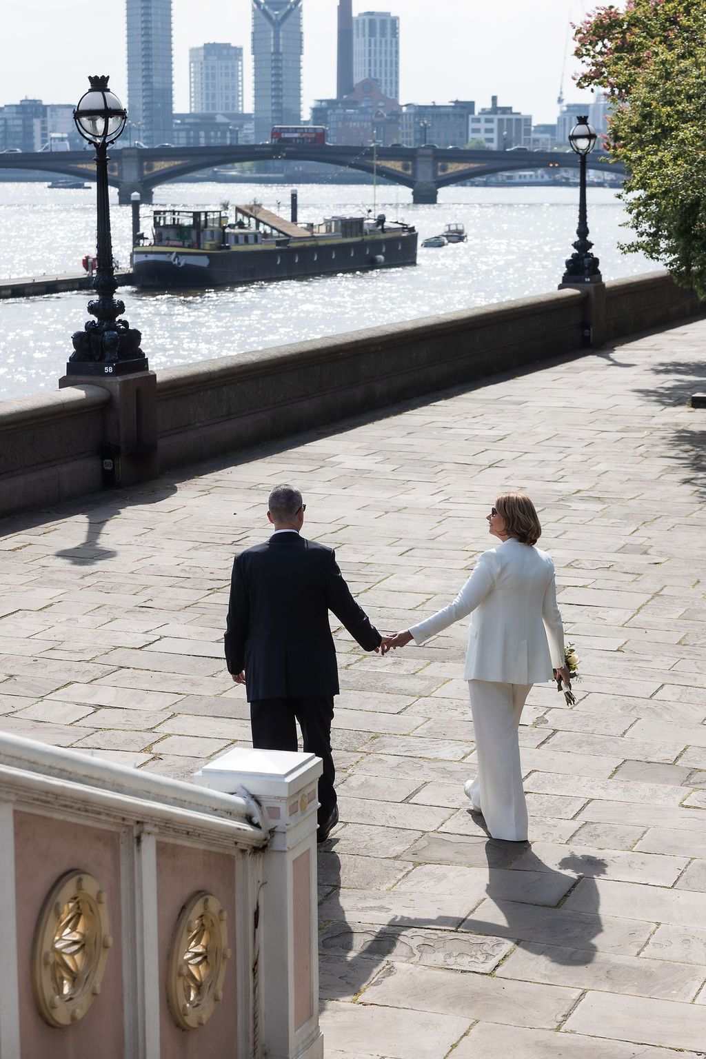 Couple walk and hold hands during couple portraits on Albert Bridge, after London Town Hall ceremony.