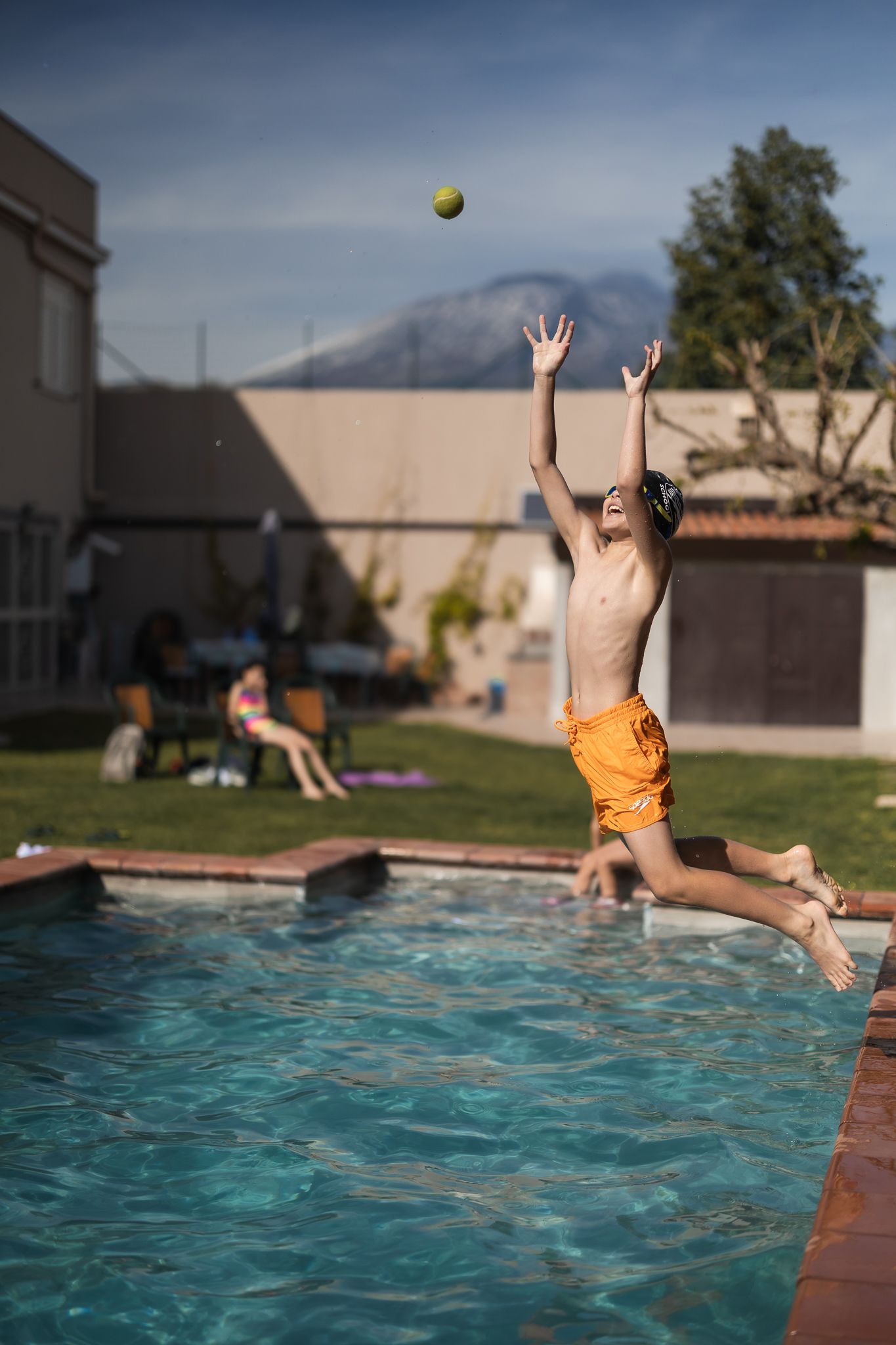 A family playing with a ball in the outdoor pool with a view of Mount Etna in the background.