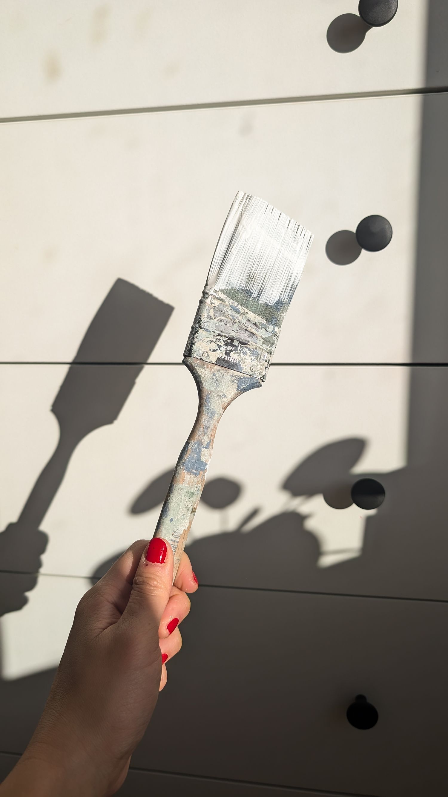 Light and shadow creating interest in a simple photo of paint brush being held up against a dresser.