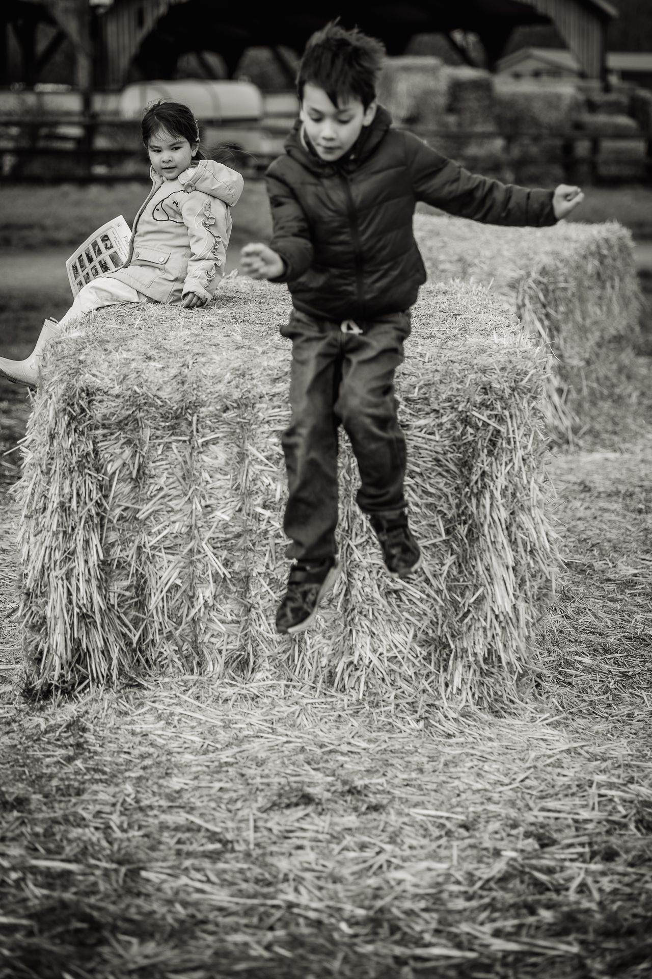 Black and white image of young boy jumping from hay bale in Hertfordshire Farm.