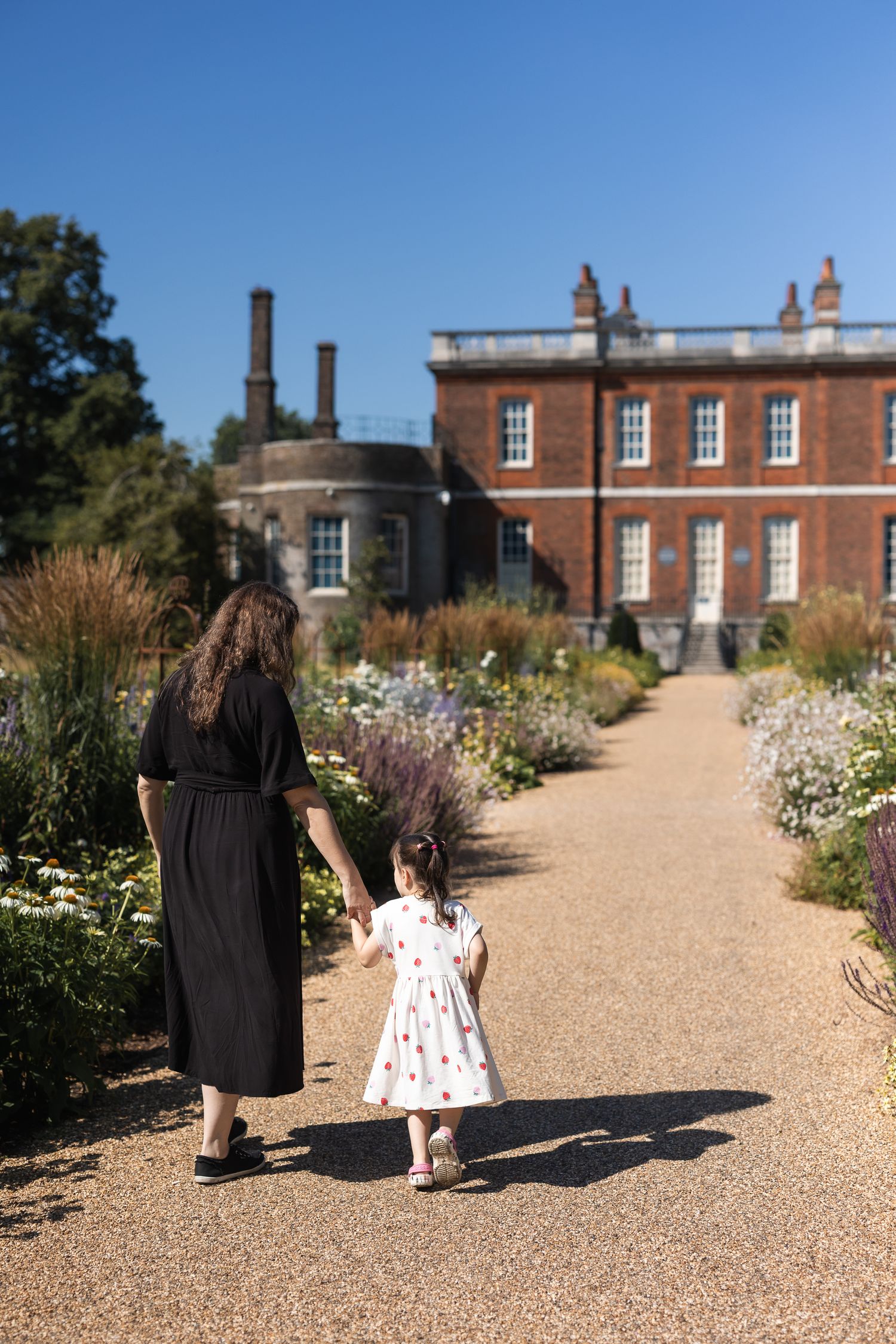 Mum and daughter walking away holding hands in Greenwich Park, South East London.