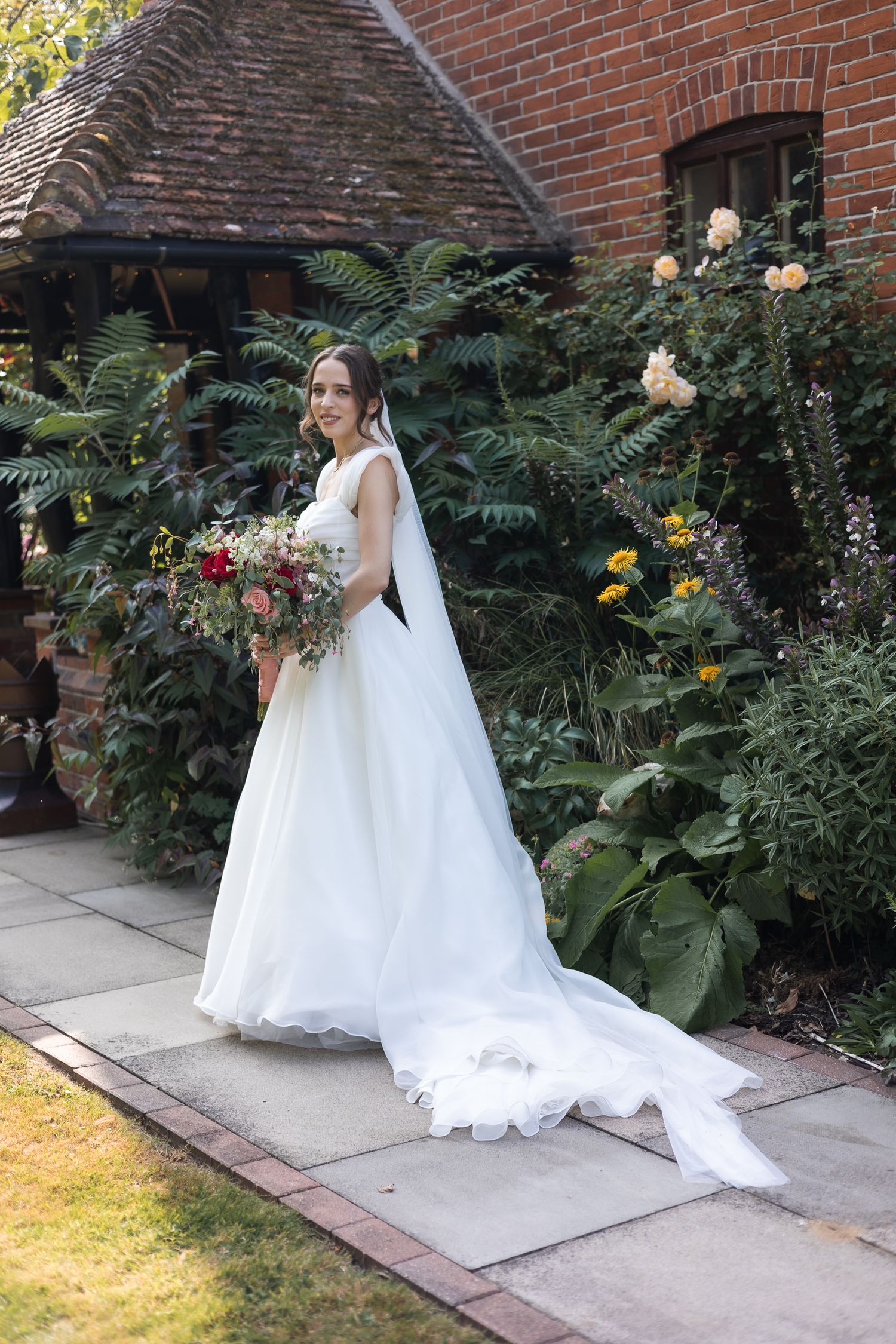 Bridal portait outside, carrying her bouquet and train of her dress trailing behind.