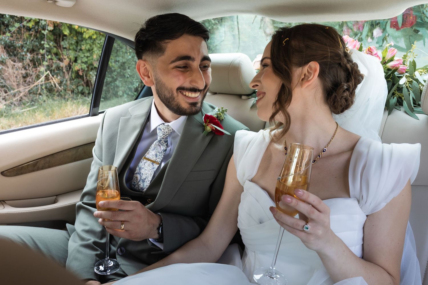 The newly weds in the wedding car about to drive to the reception, holding a glass of champagne each.