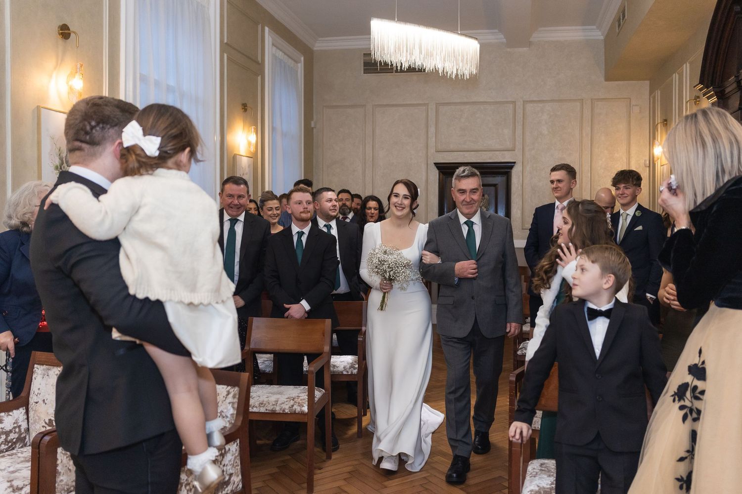 Father of the bride walks his daughter down the aisle in Harrington Room at Chelsea Old town hall.