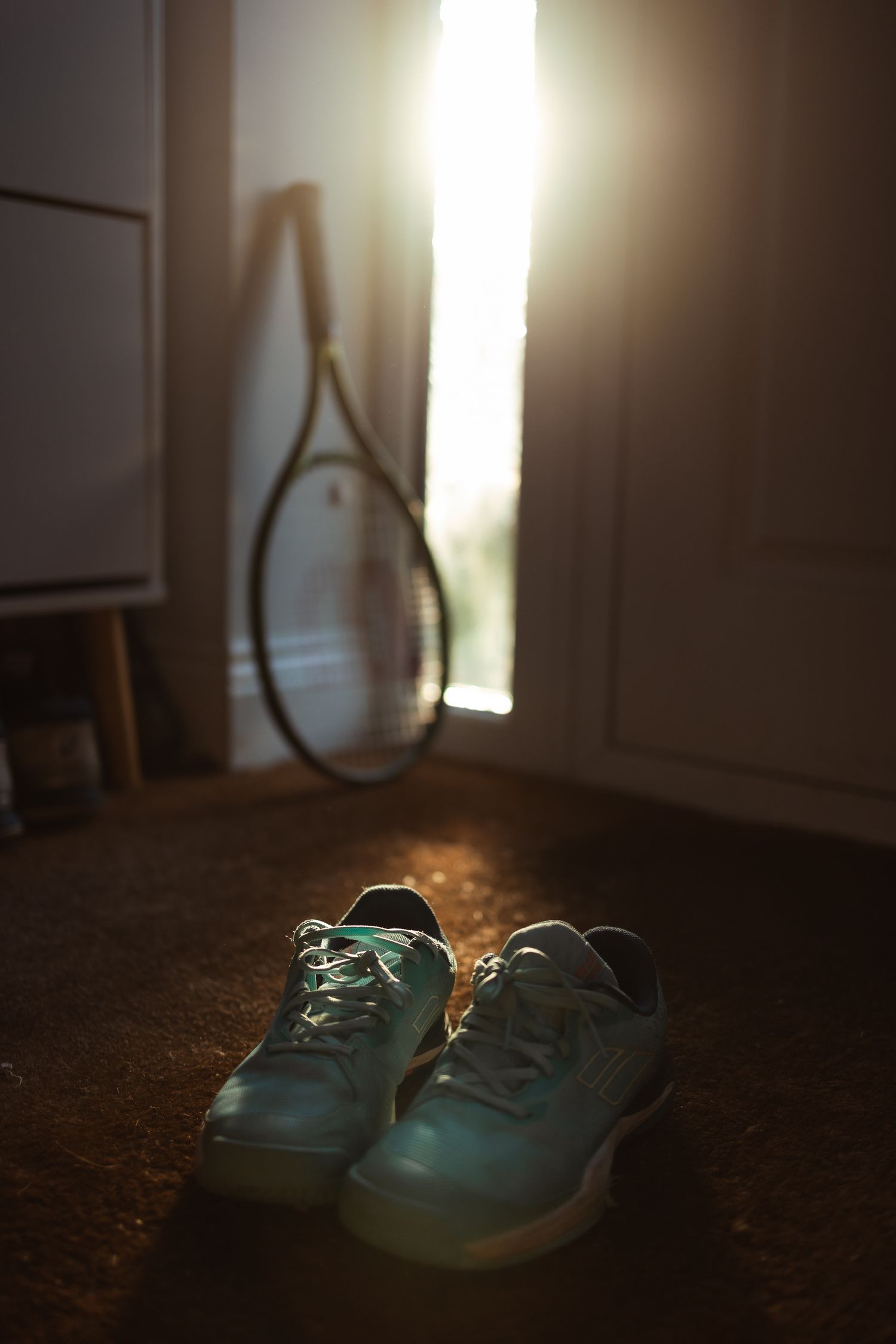The evening light coming through the porch of the house, highlighting tennis racket and shoes lying on the floor.