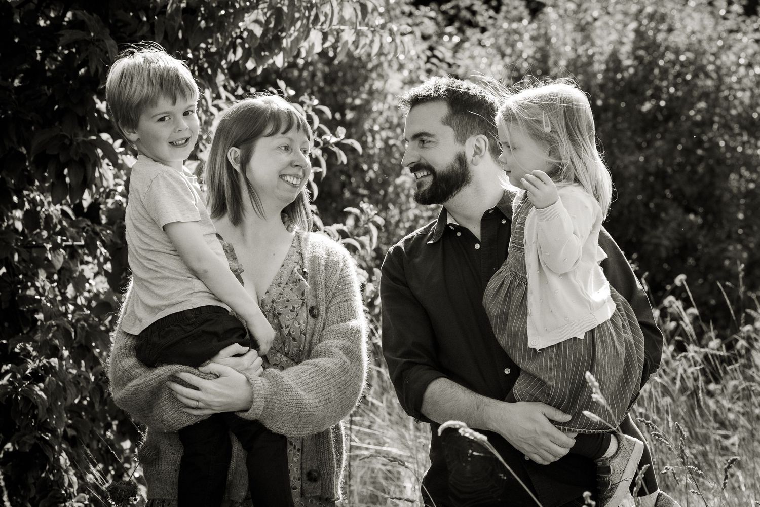 Black and white image of a family of 4 laughing and joking with each other.