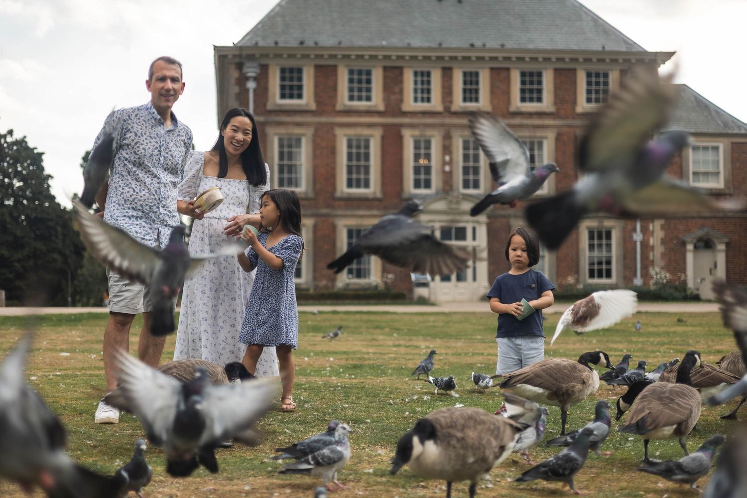 Family stood in front of Forty Hall, Enfield. Parents are watching on as children run around, and the birds flying around them.