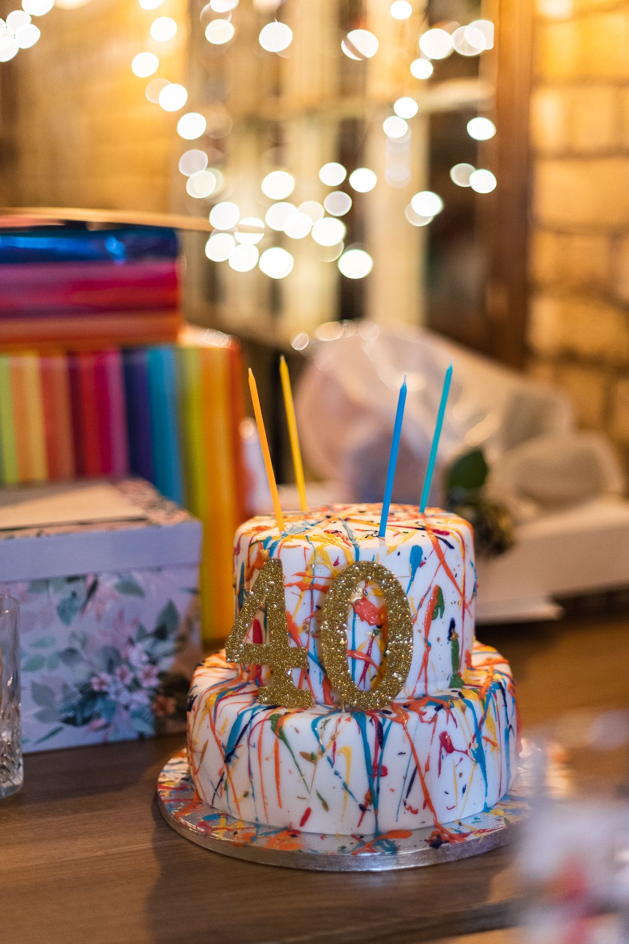 Birthday cake in the foreground, with wrapped presents, gift bags and fairy lights in the background.