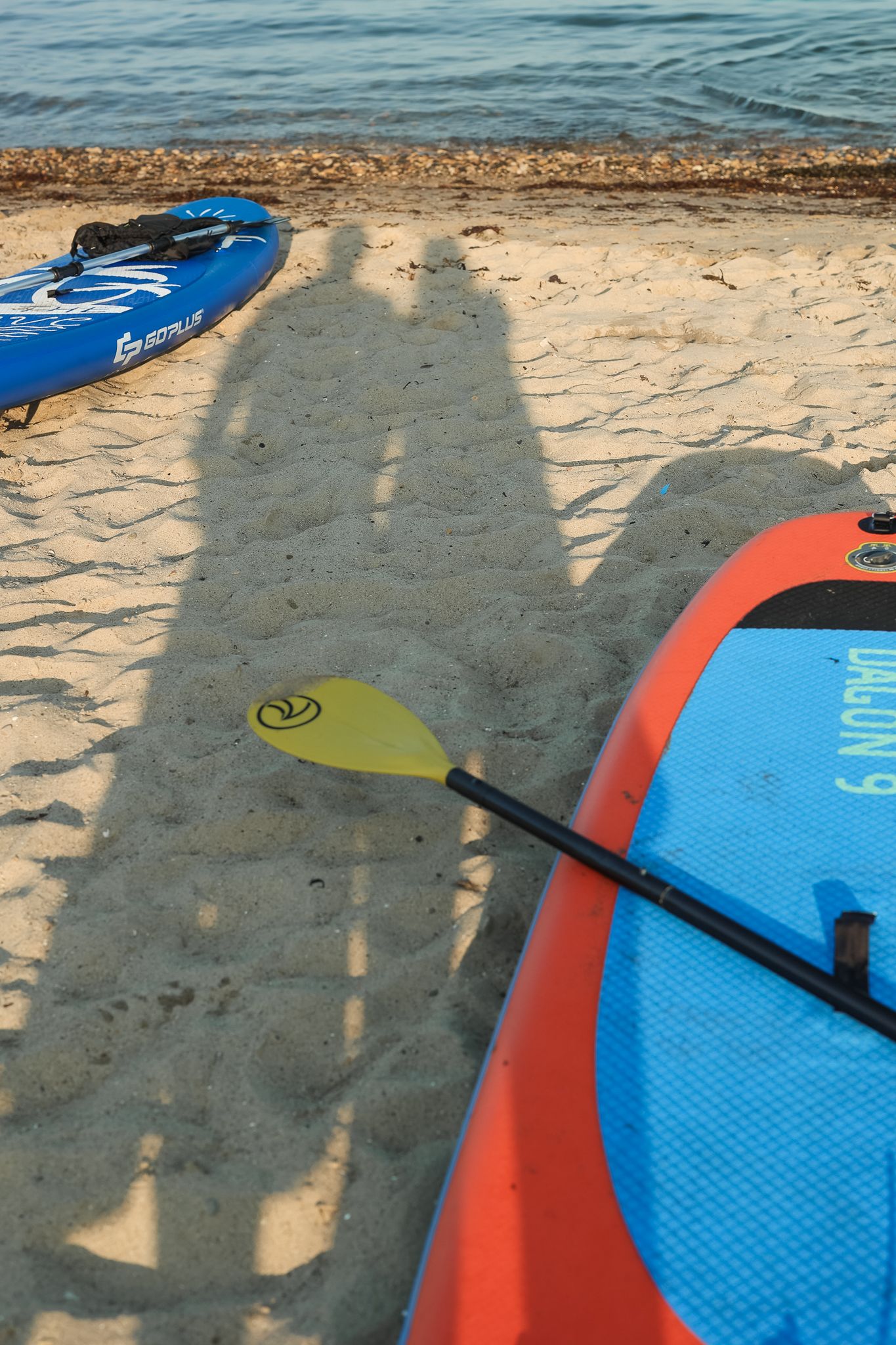 Long afternoon shadows of me and my husband cast on the sandy Aberdour beach, surrounded by kayaks.