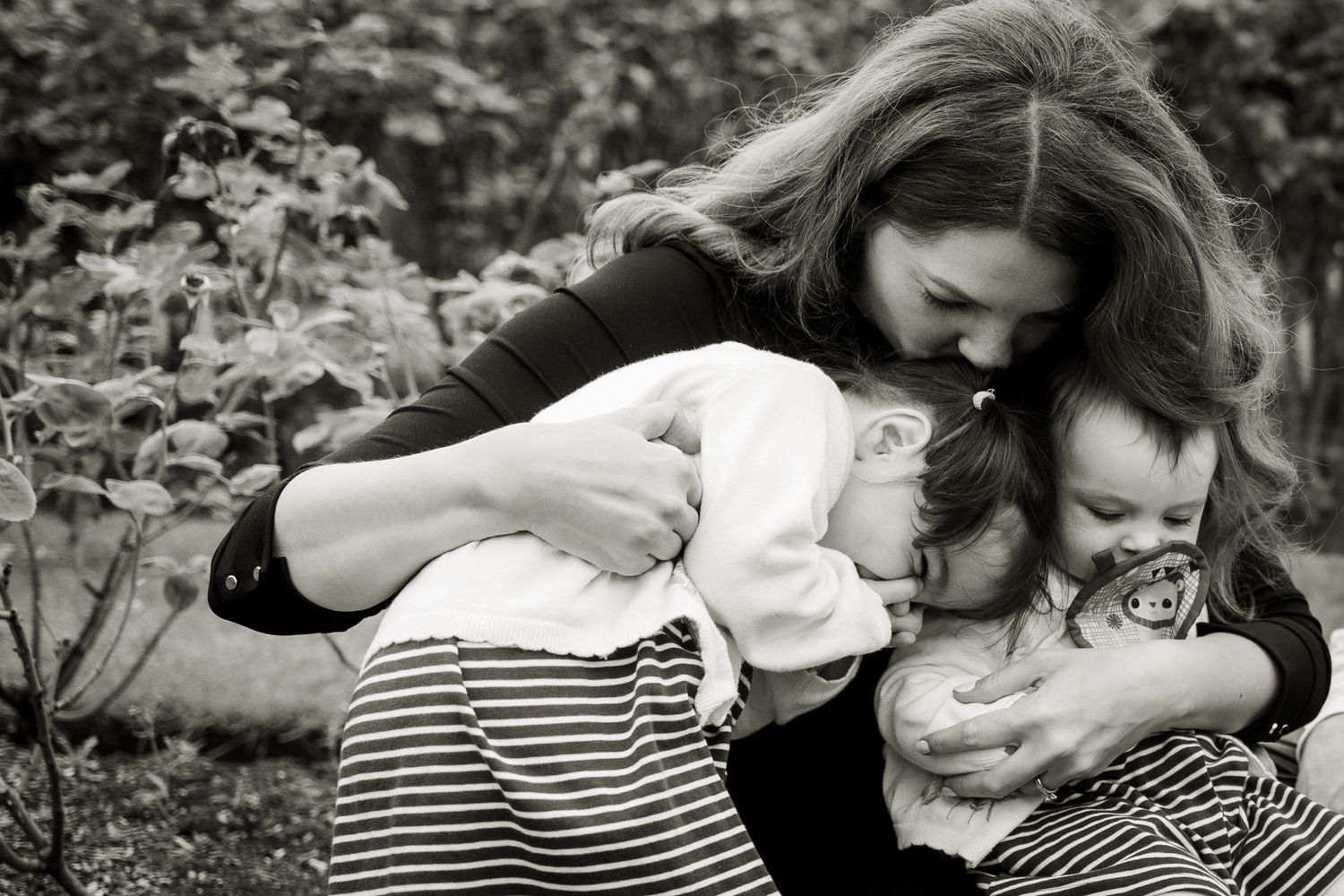 Black and white image of a mum giving her two daughters a giant bear hug.