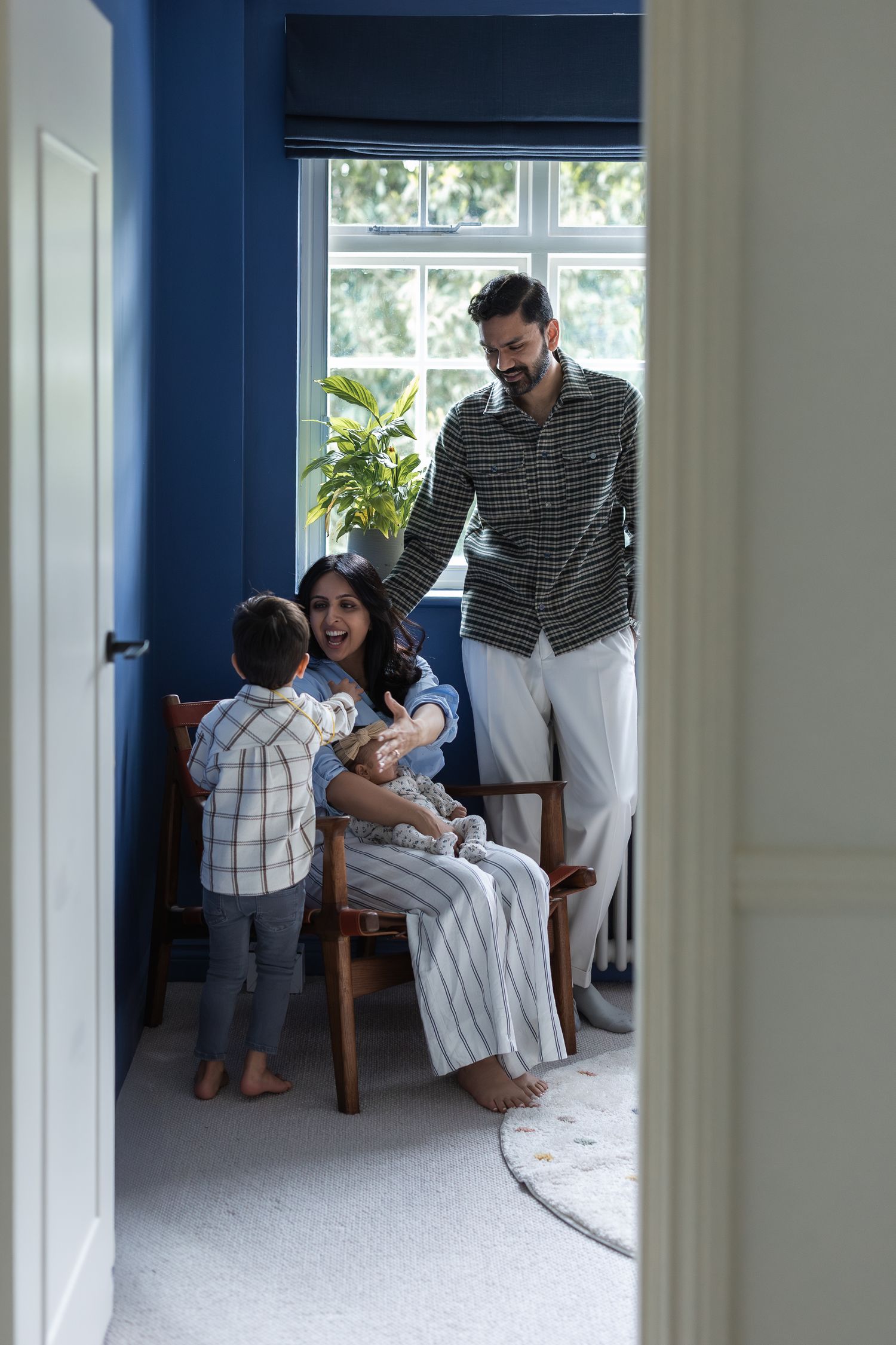 Intimate image of a family of 4 through the doorway, on an at-home family shoot in Mill Hill.