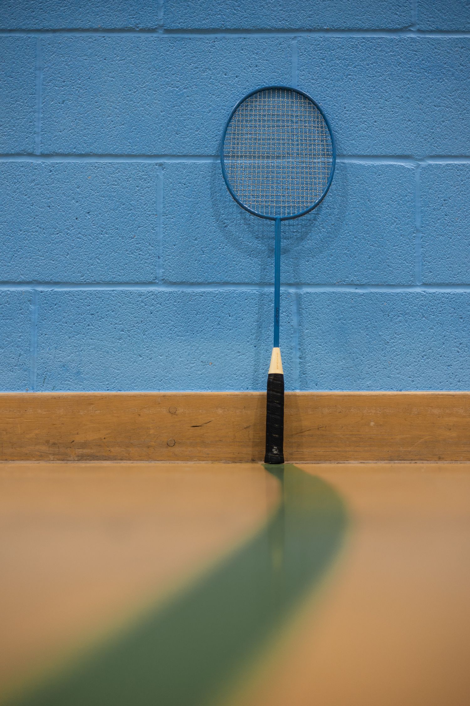Clean lines and negative space showing a badminton racket standing up against the wall.