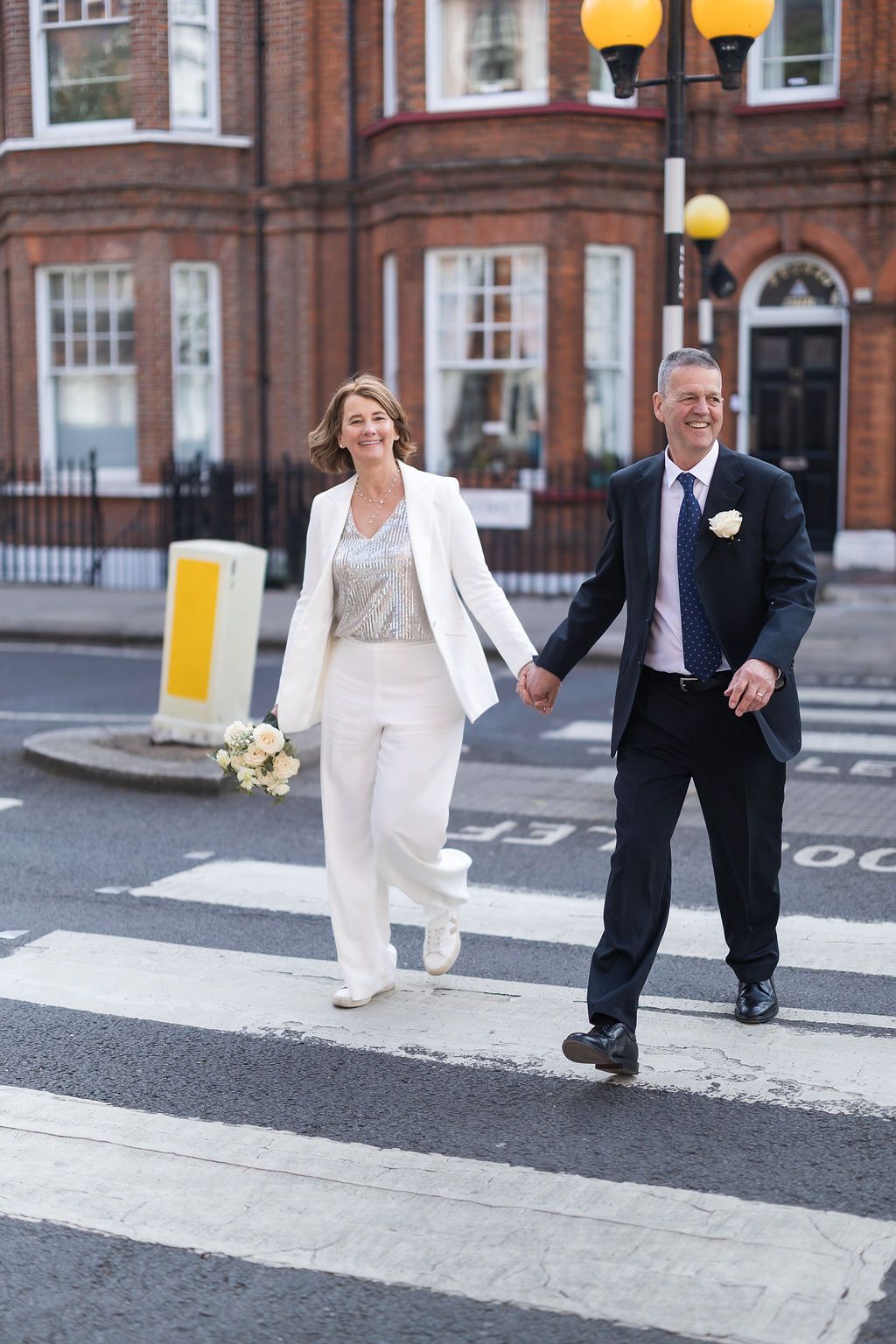 Relaxed couple hold hands as they casually cross the zebra crossing after wedding ceremony at Town hall wedding in London.
