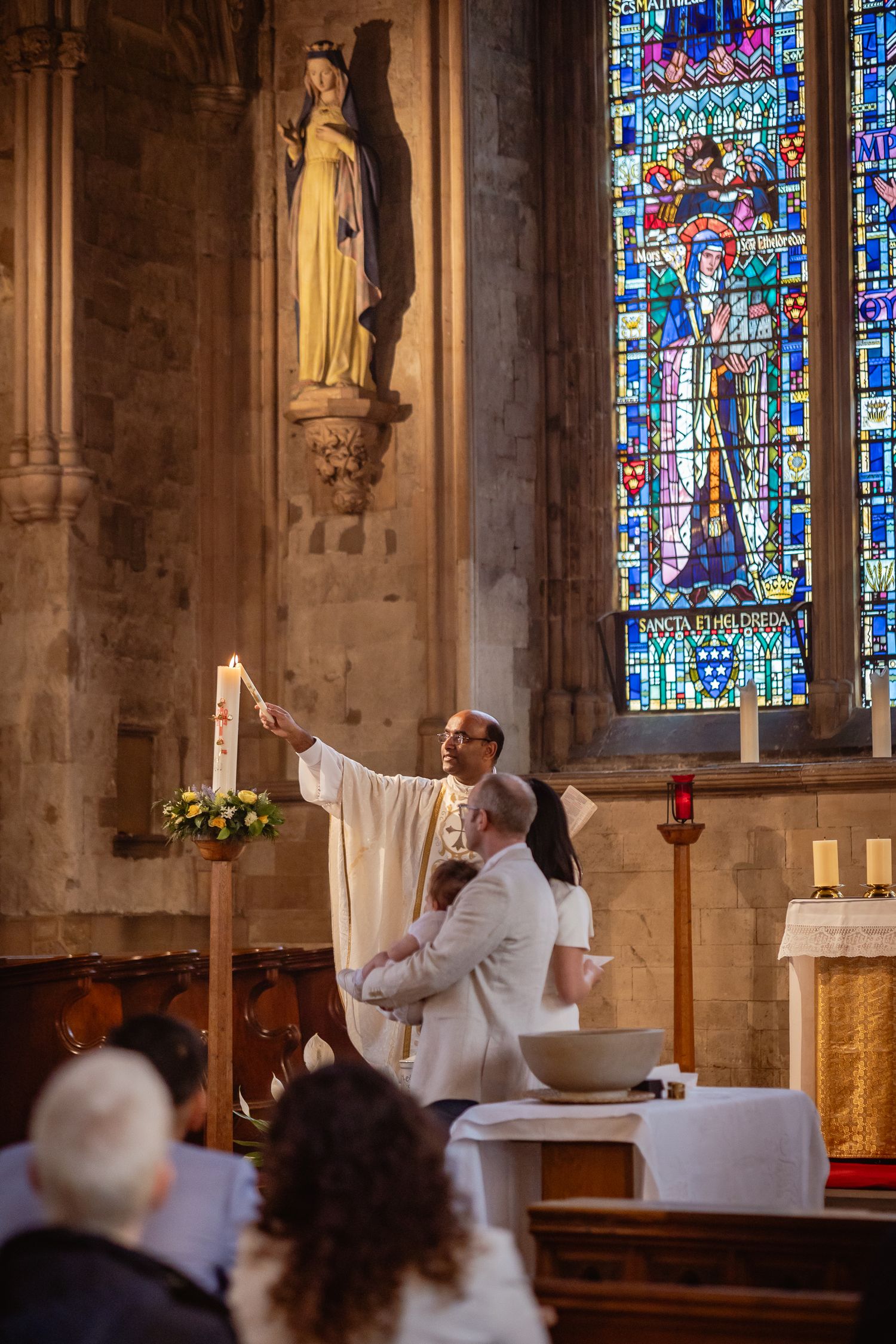 At a Christening with the priest reaching up high to light the Baptism candle from the main candle on the altar.