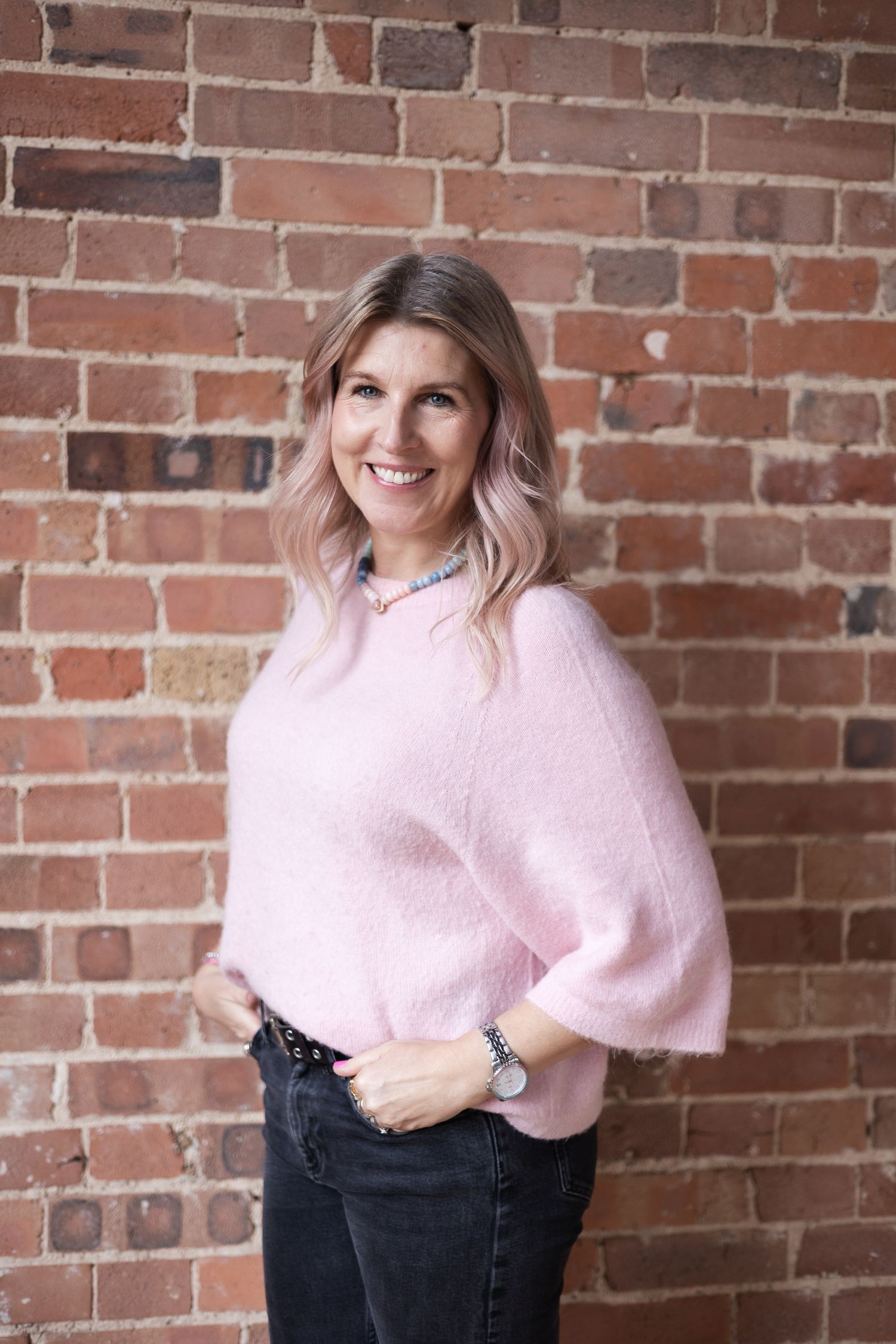 Soft, natural headshot with gentle side light in studio setting with brick wall as backdrop.