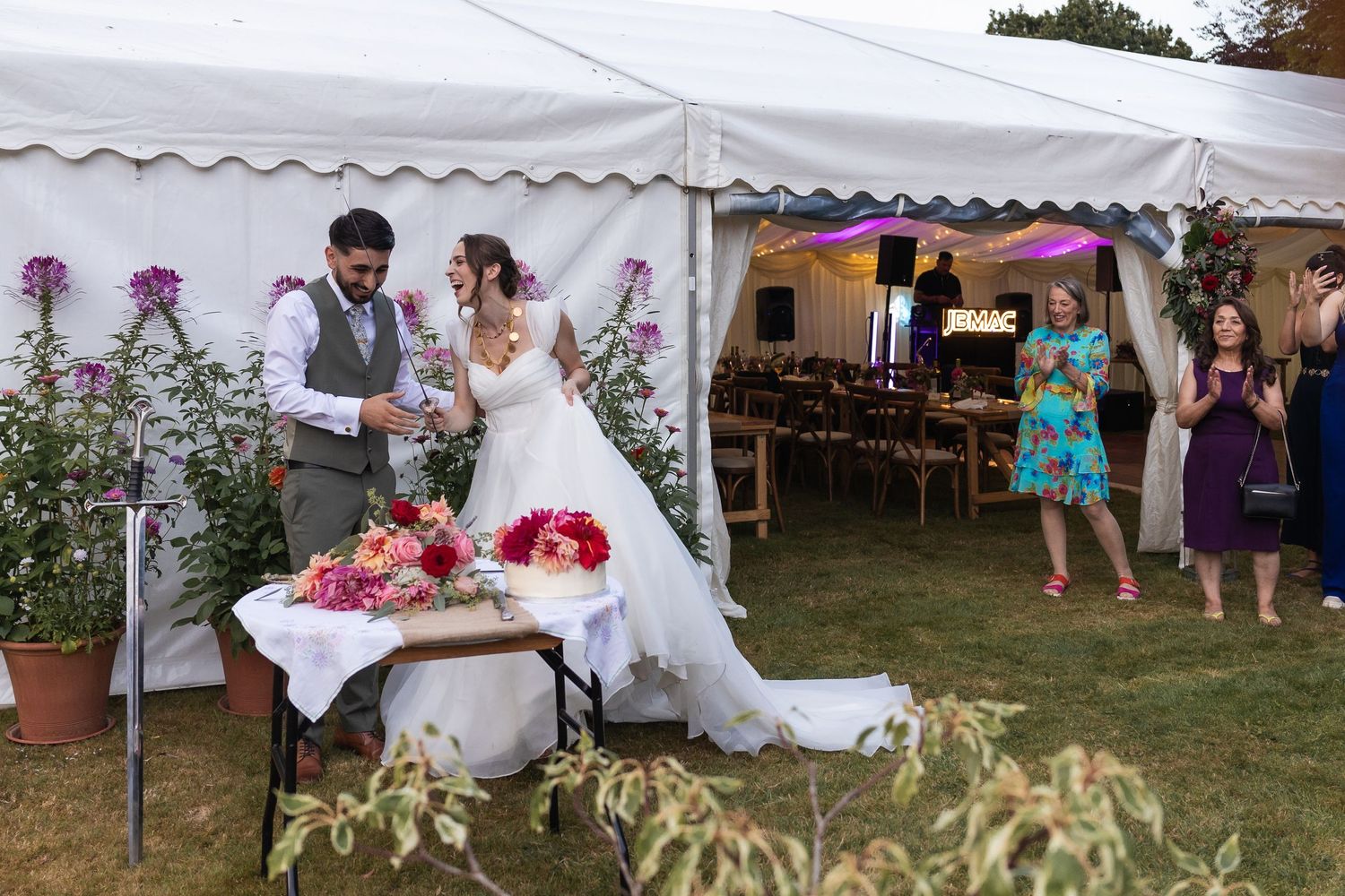 Wide angle of the bride and groom attempt to cut the cake with a sword causing much hilarity.
