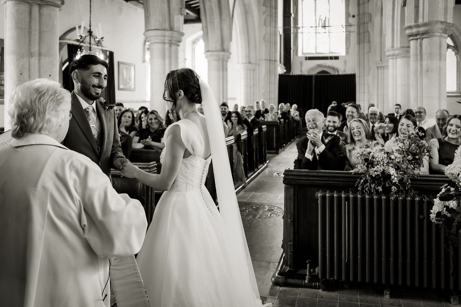 The bride and groom exchanging vows in the church, whilst the guests look on from the pews.