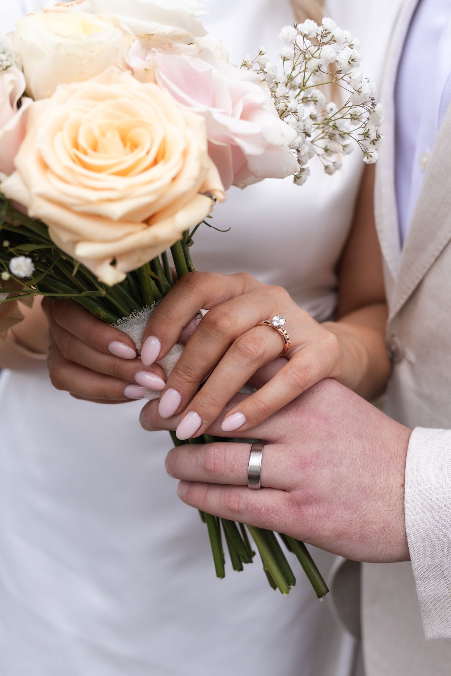 Close up image of a bride and grooms hands, showing off their new wedding rings, and the bridal bouquet.