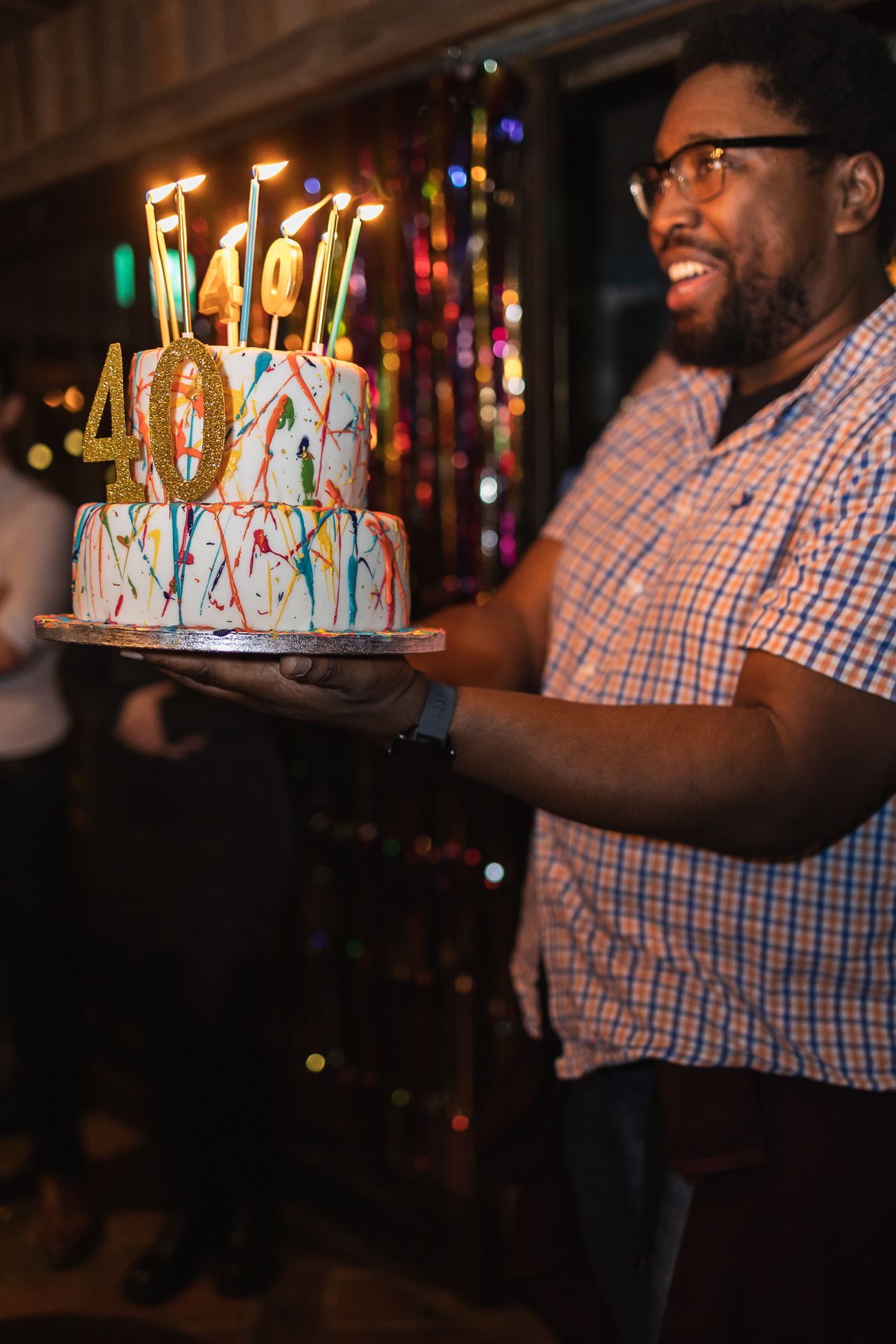 At a 40th birthday party event in Richmond, London. The birthday cake, lit with candles is being brought out.