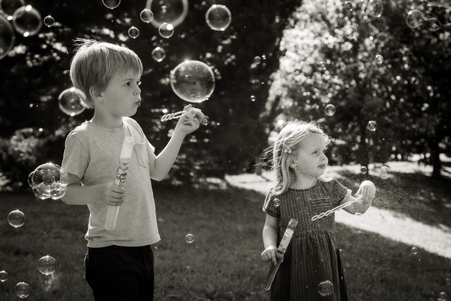 Two young children blowing bubbles outside, with the sun shining, on a photoshoot in Hampstead Heath.