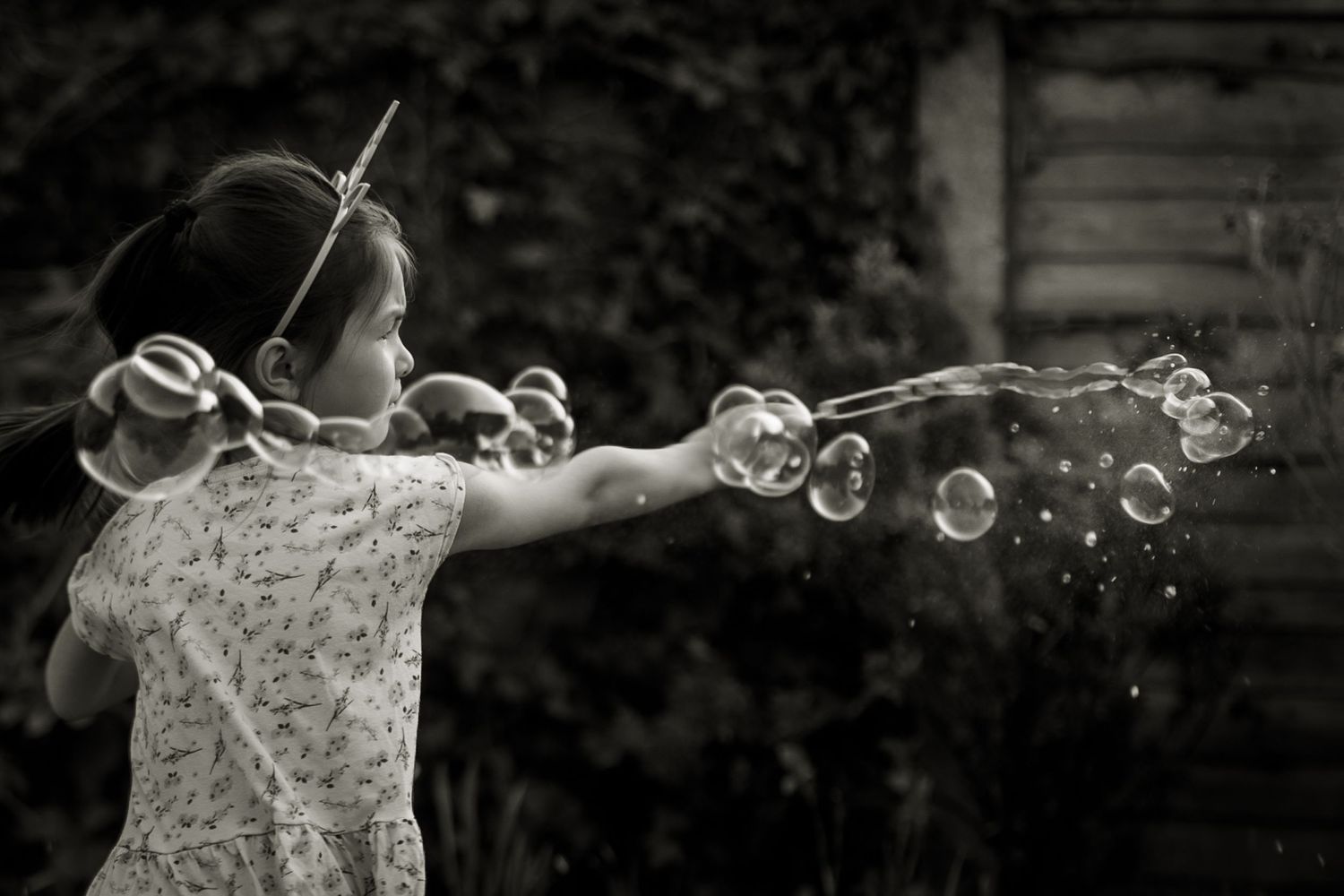 Black and white image of young girl playing with bubbles. A string of bubbles across the photo.