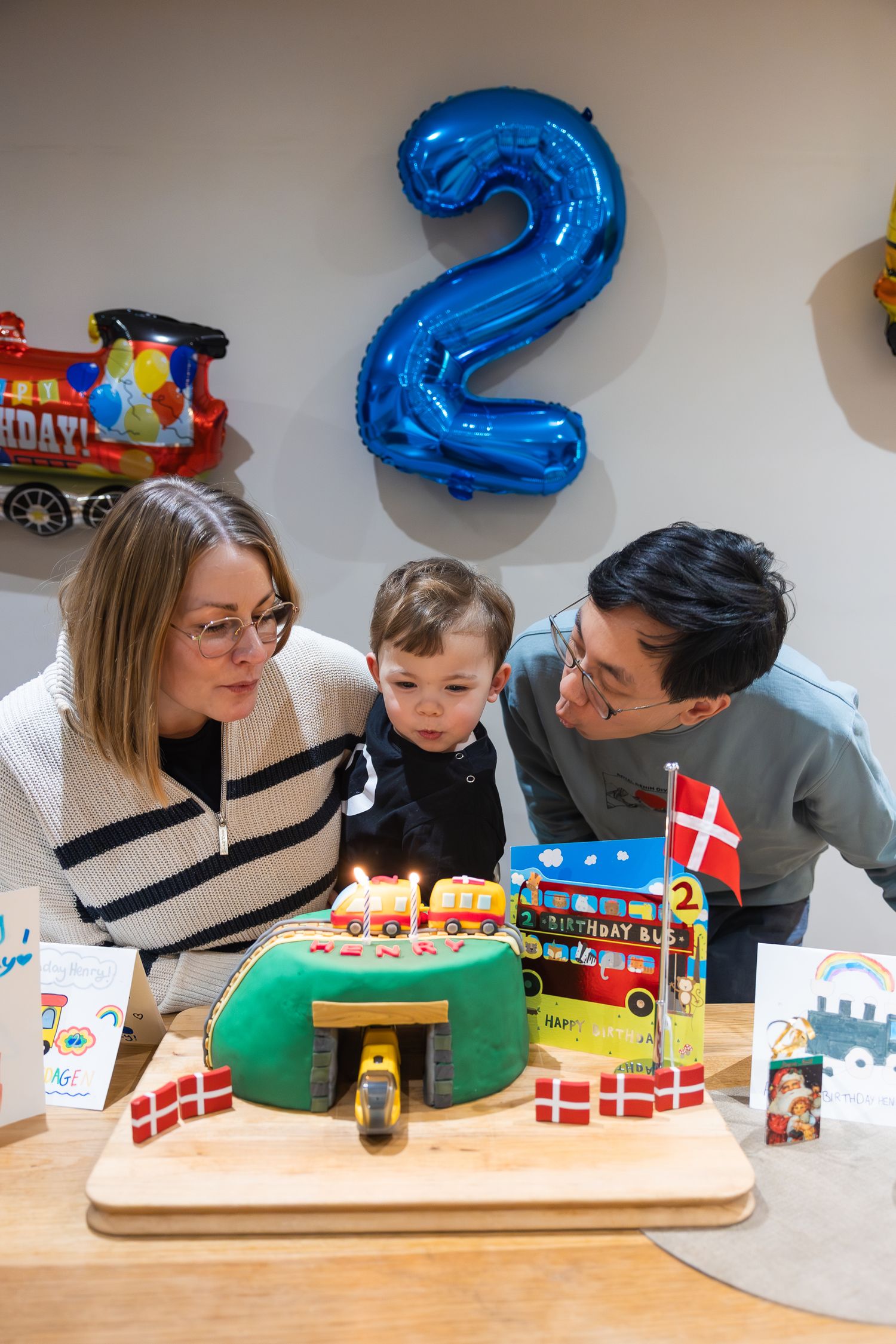 At a 2 year old birthday party. Photo of the mum, dad and birthday boy blowing out the candles on his train birthday cake.