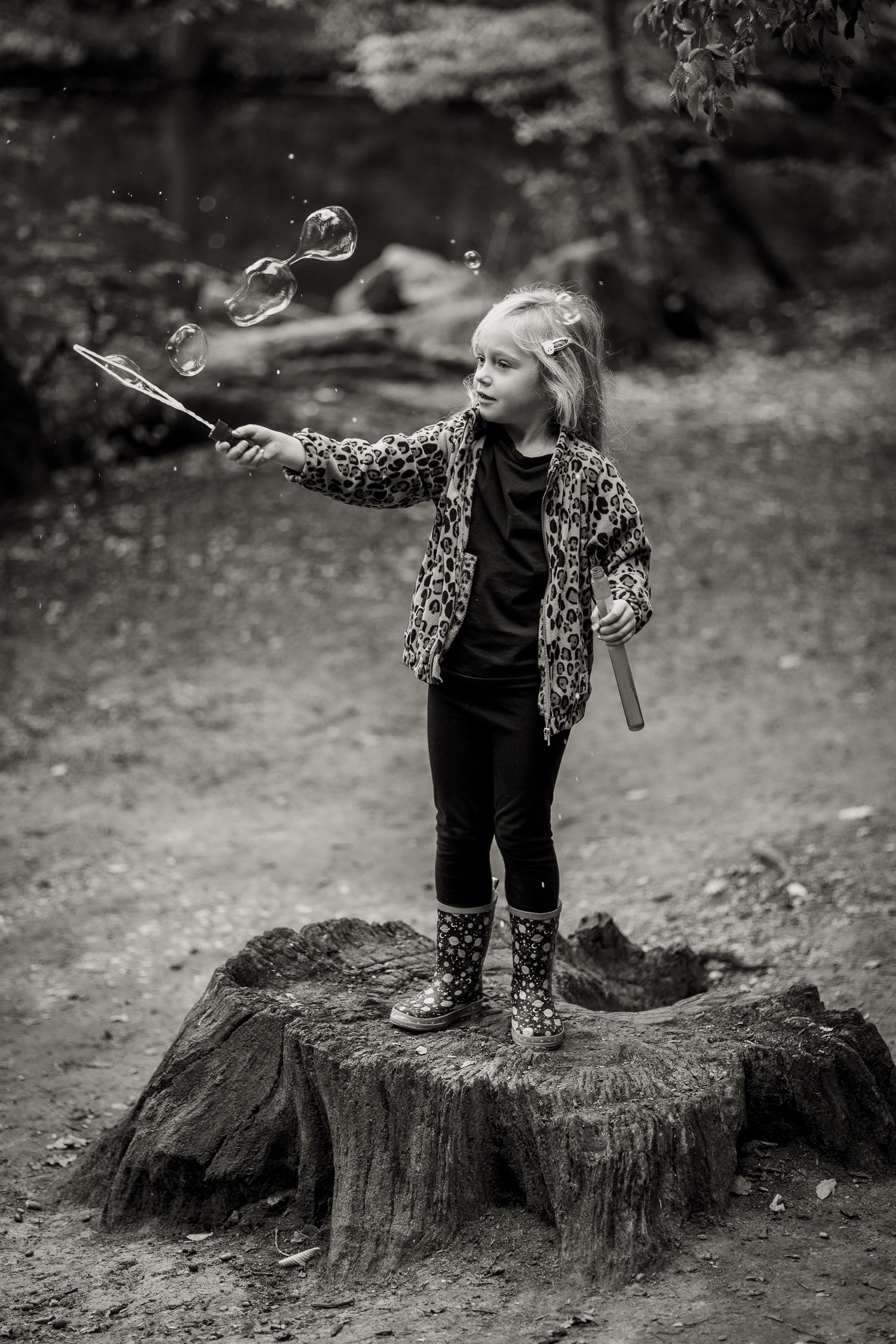 Photo of an adventurous girl standing on a tree stump in Higham's Park blowing bubbles.