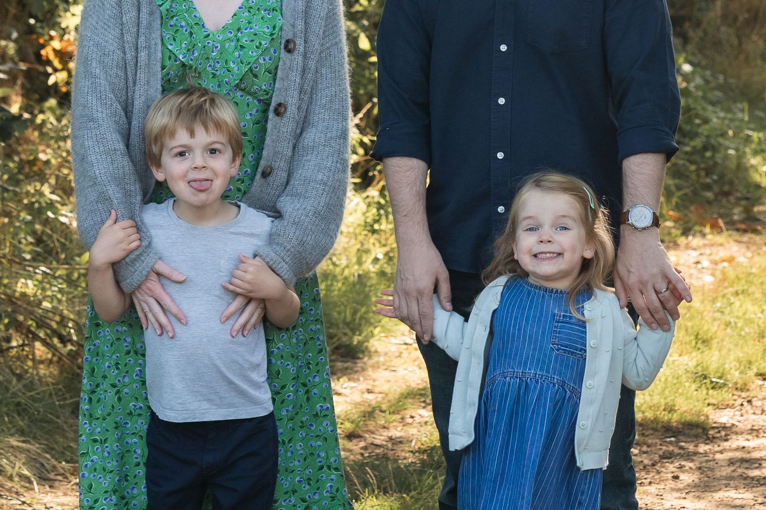 Image of a mum and dad, with their children standing infront of them making grimaces. Wes Anderson style image.