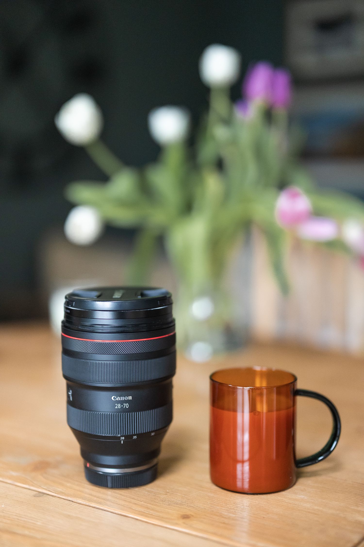 The 28-70mm F2 lens next to a mug for size comparison, with a bunch of tulips in the background.