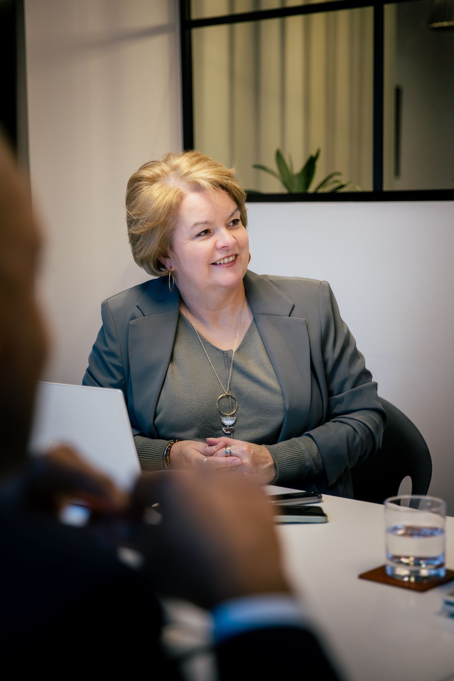 Professional woman in gray blazer smiling during a business meeting at a conference table.