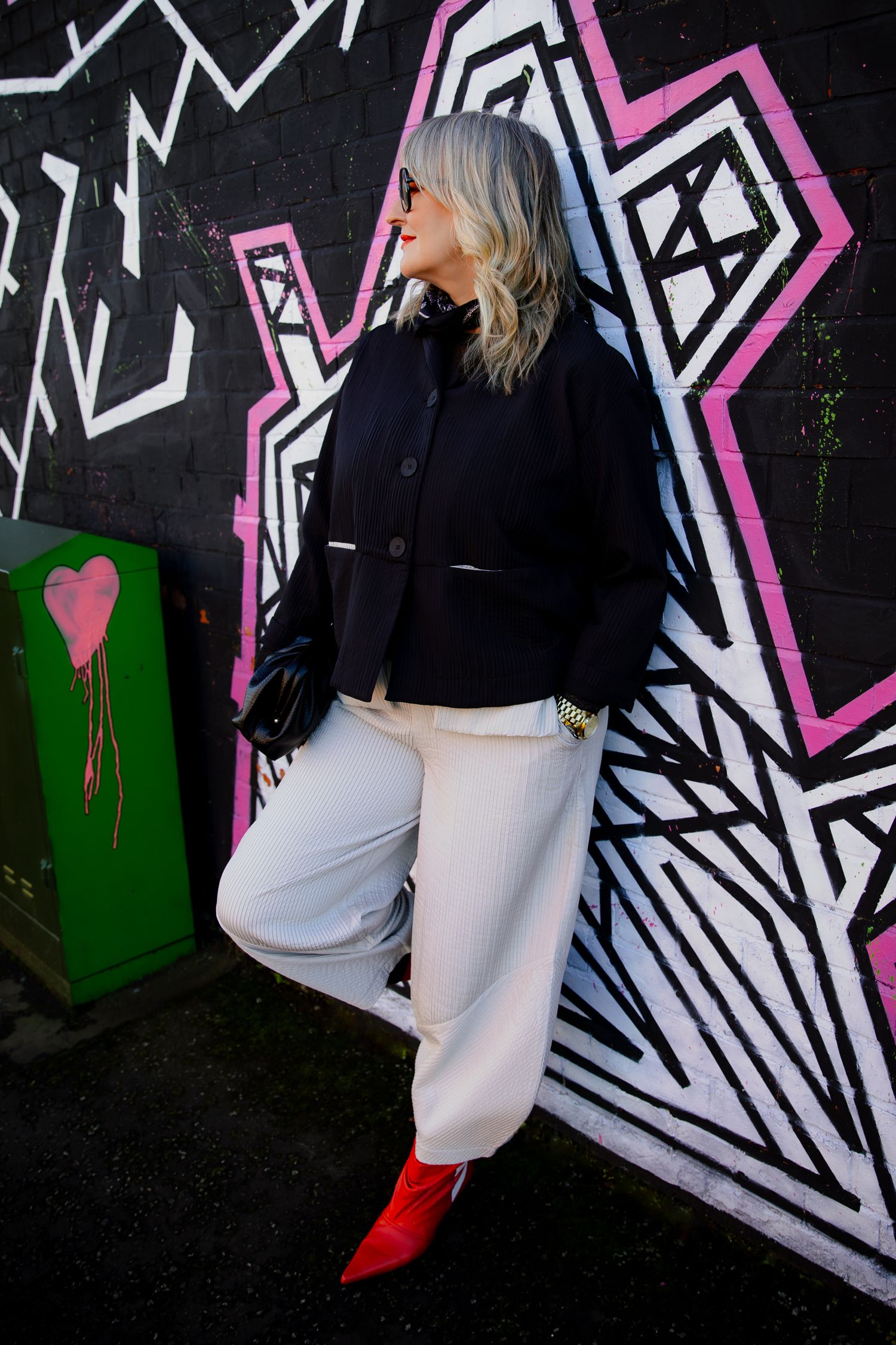 Stylish woman in navy jacket, white pants, and red boots posing against vibrant graffiti wall.