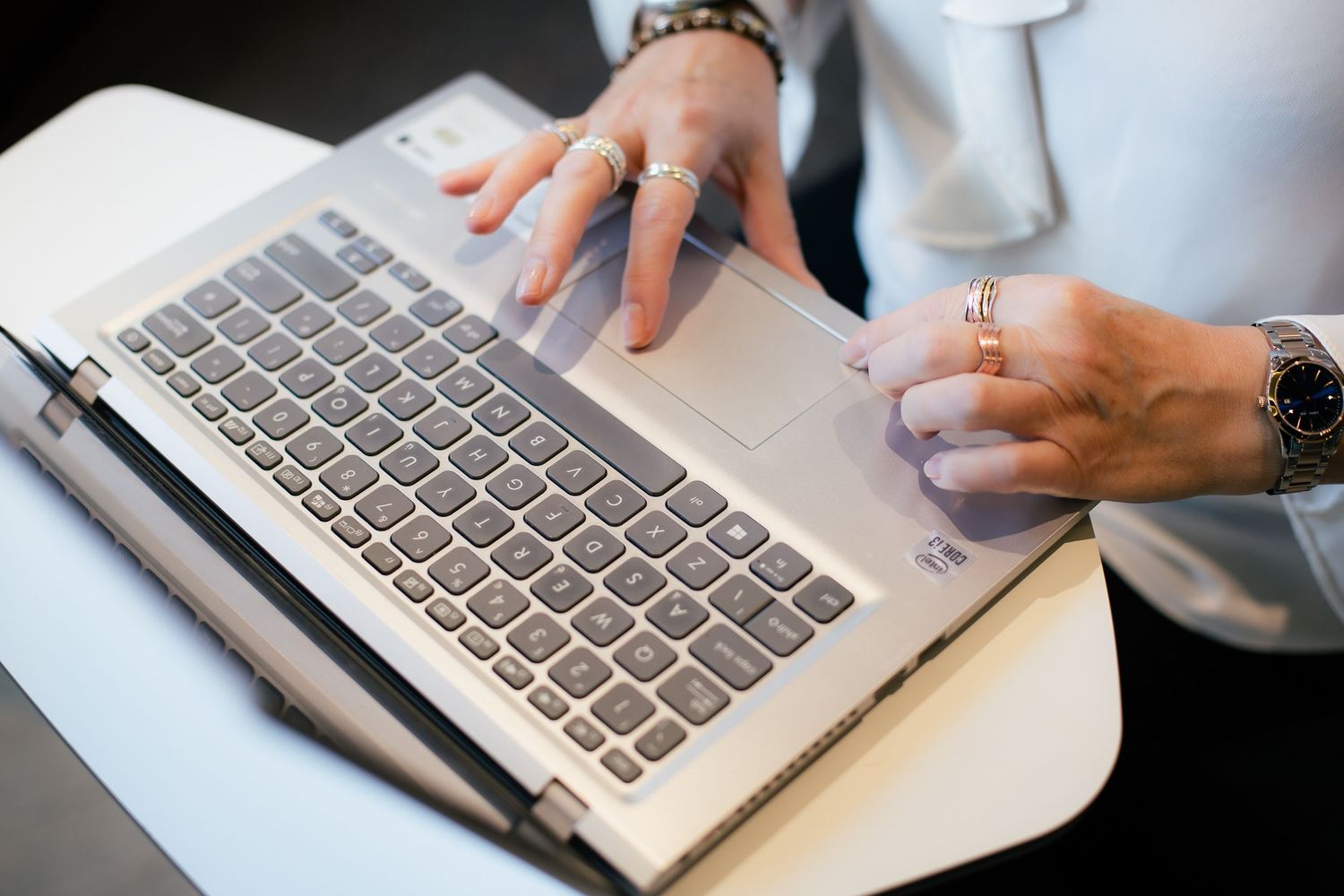 Close-up of hands with rings typing on a silver Lenovo laptop keyboard on a white desk.