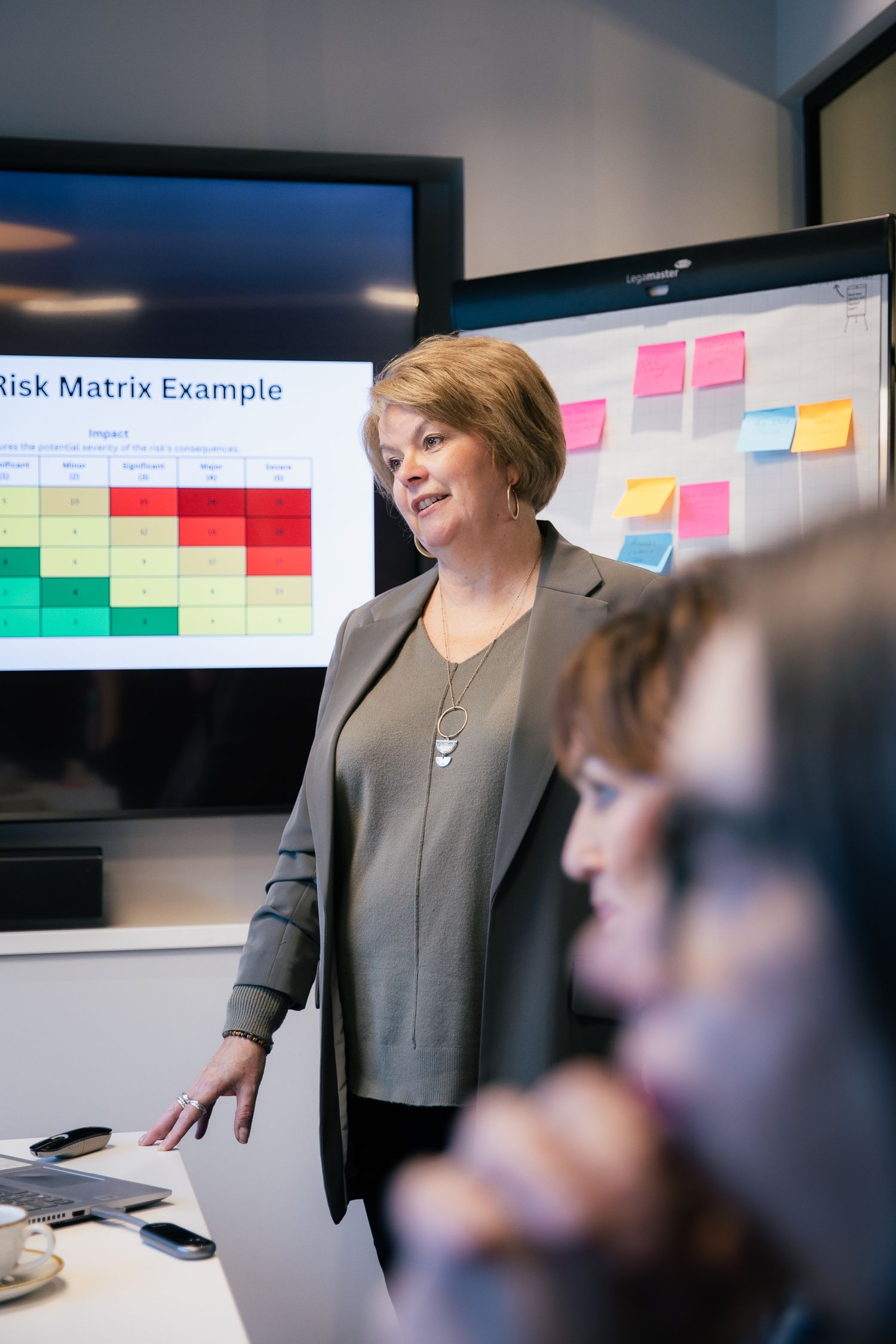 Professional woman presenting a Risk Matrix Example on a screen during a business meeting with colleagues.