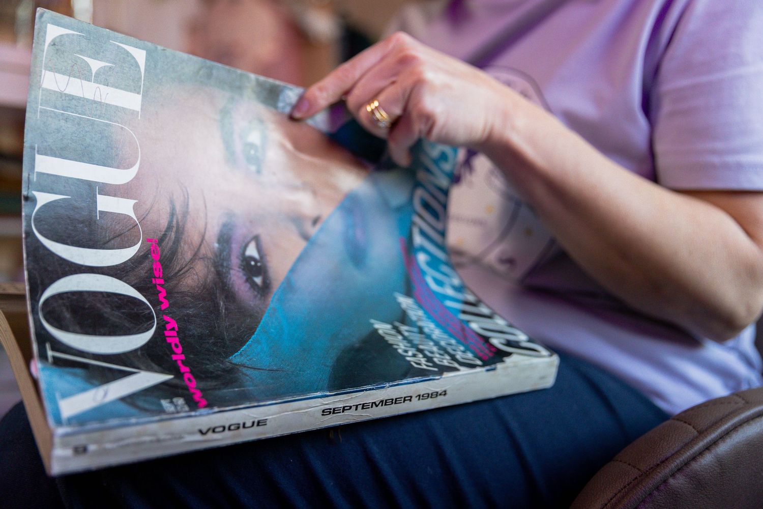 Person holding a Vogue magazine September issue, showing a close-up cover portrait while relaxing on a sofa.