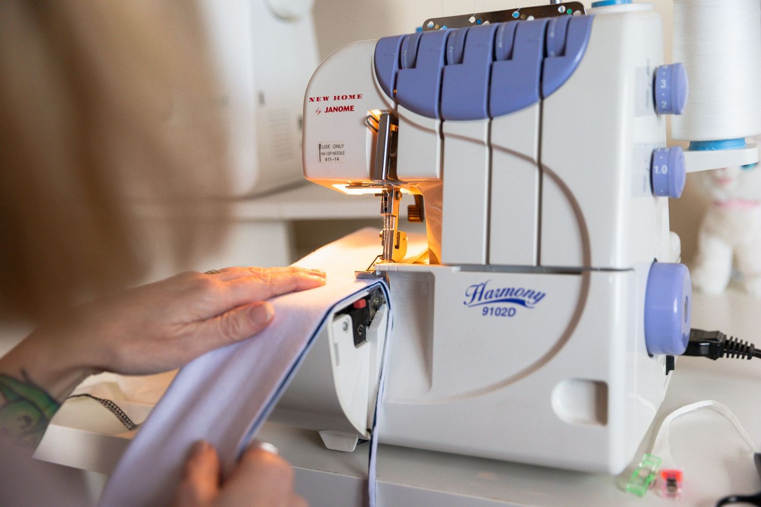 Woman sewing fabric on a Harmony overlocker sewing machine with bright illumination in a craft studio.