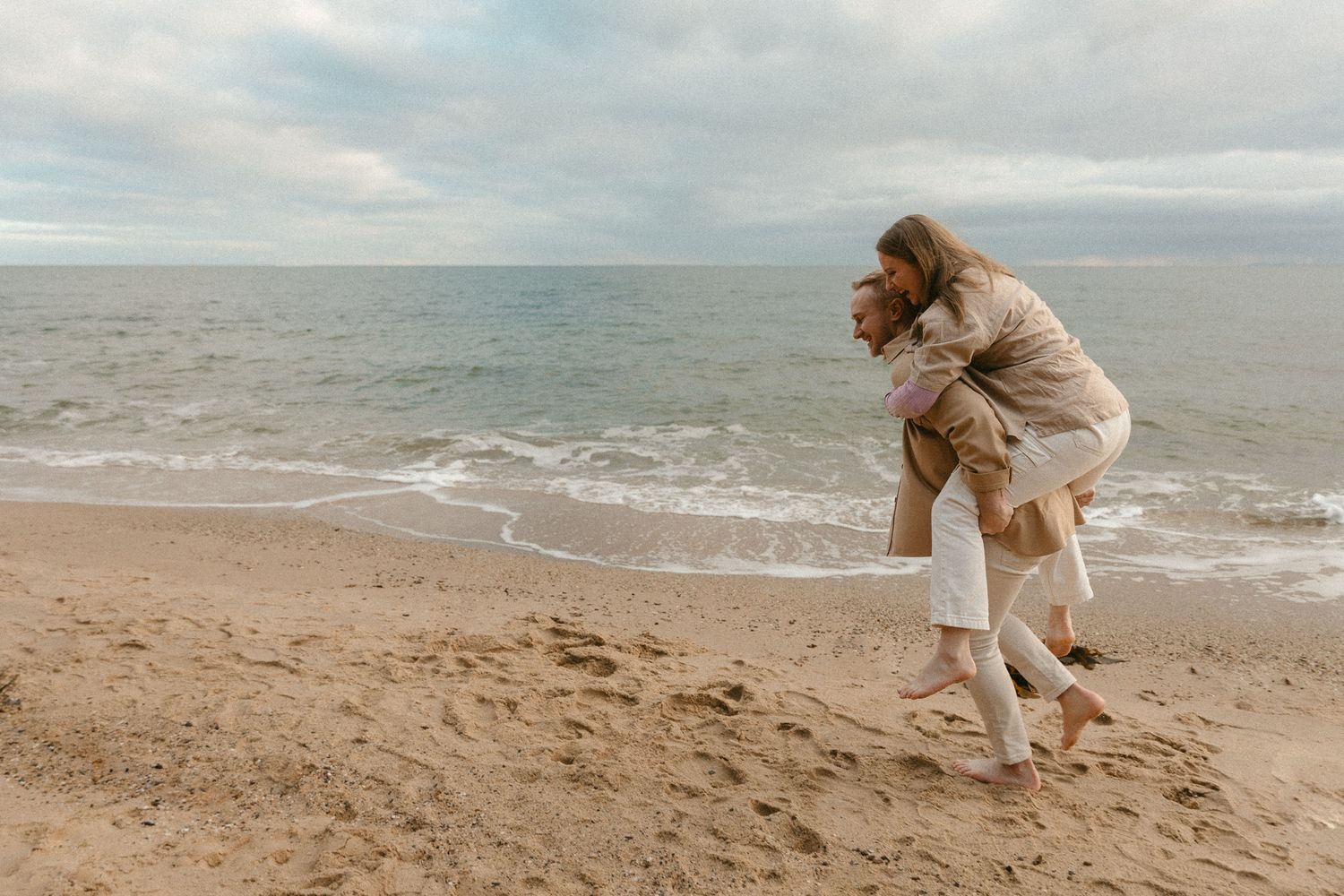 A playful piggyback ride on a cloudy beach with waves in the background.