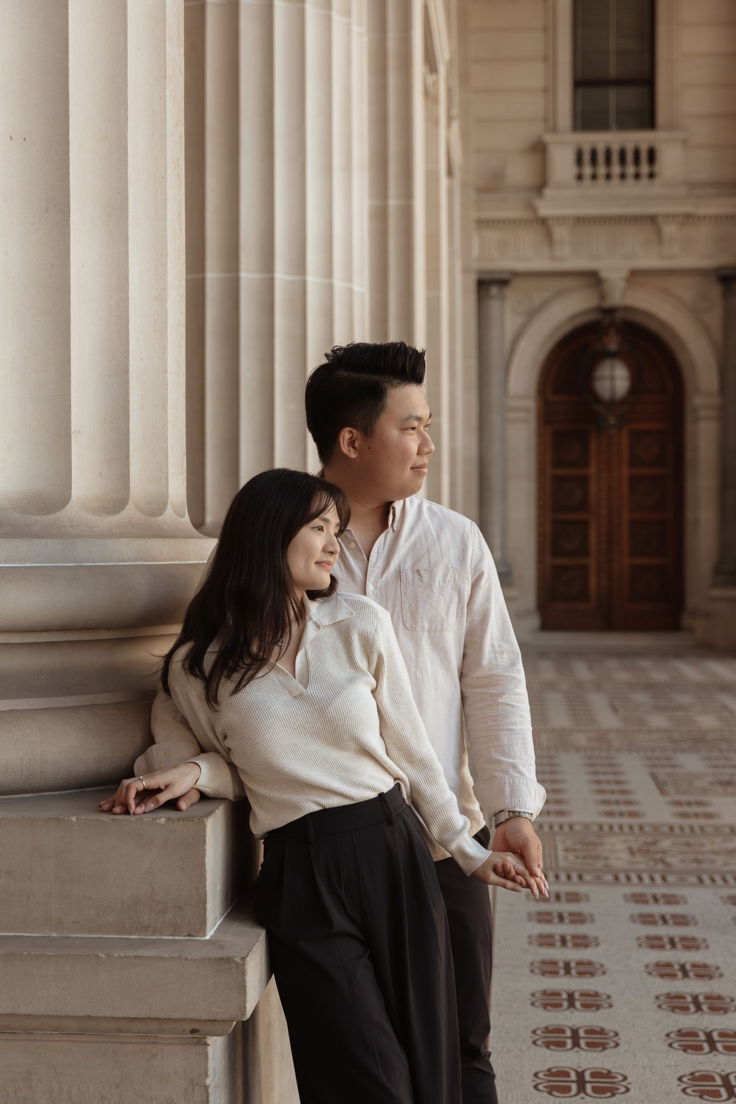 A couple poses against grand stone columns in coordinated black and white outfits.