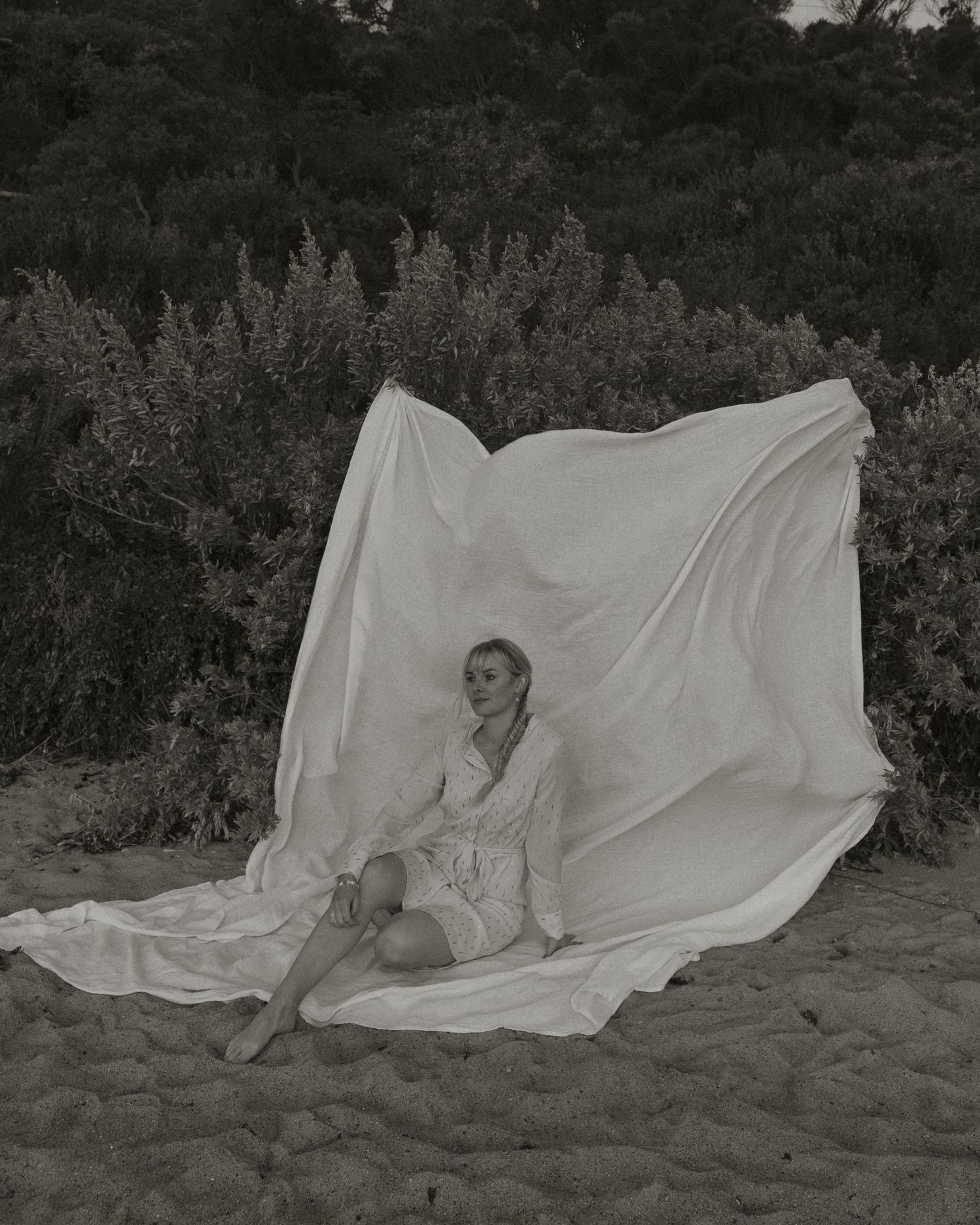 Artistic black and white portrait with flowing white fabric against nature backdrop.