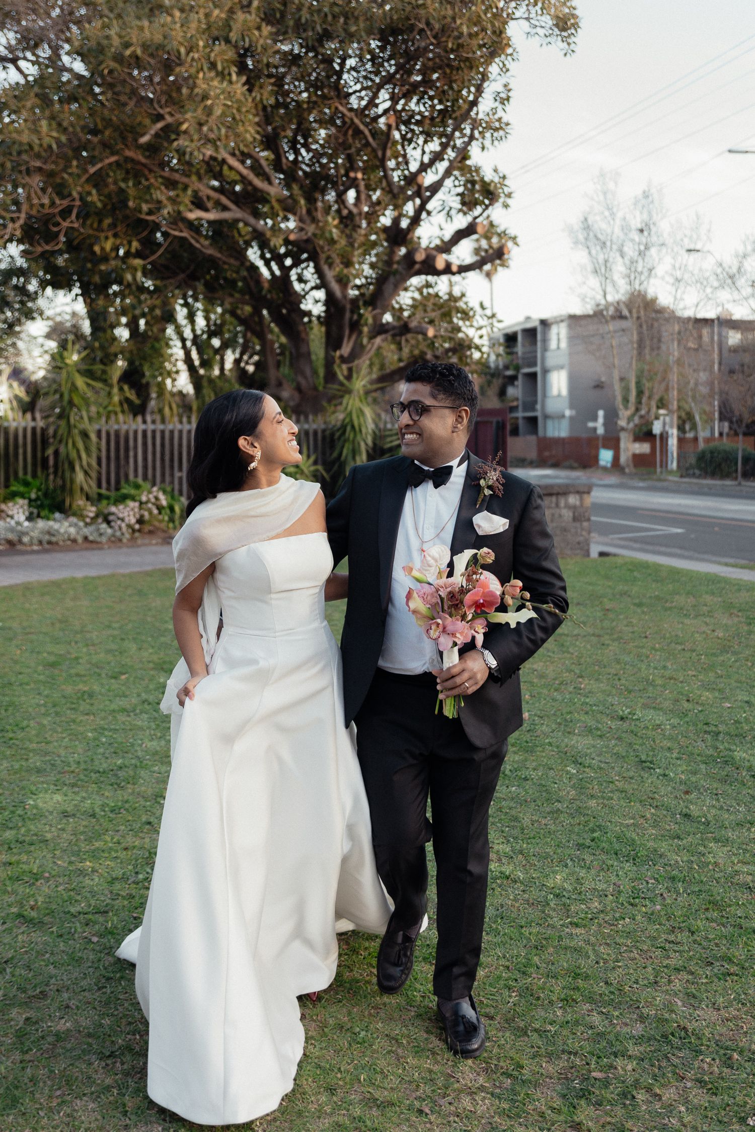 A couple shares a happy moment on their wedding day in a garden setting while wearing traditional wedding attire.
