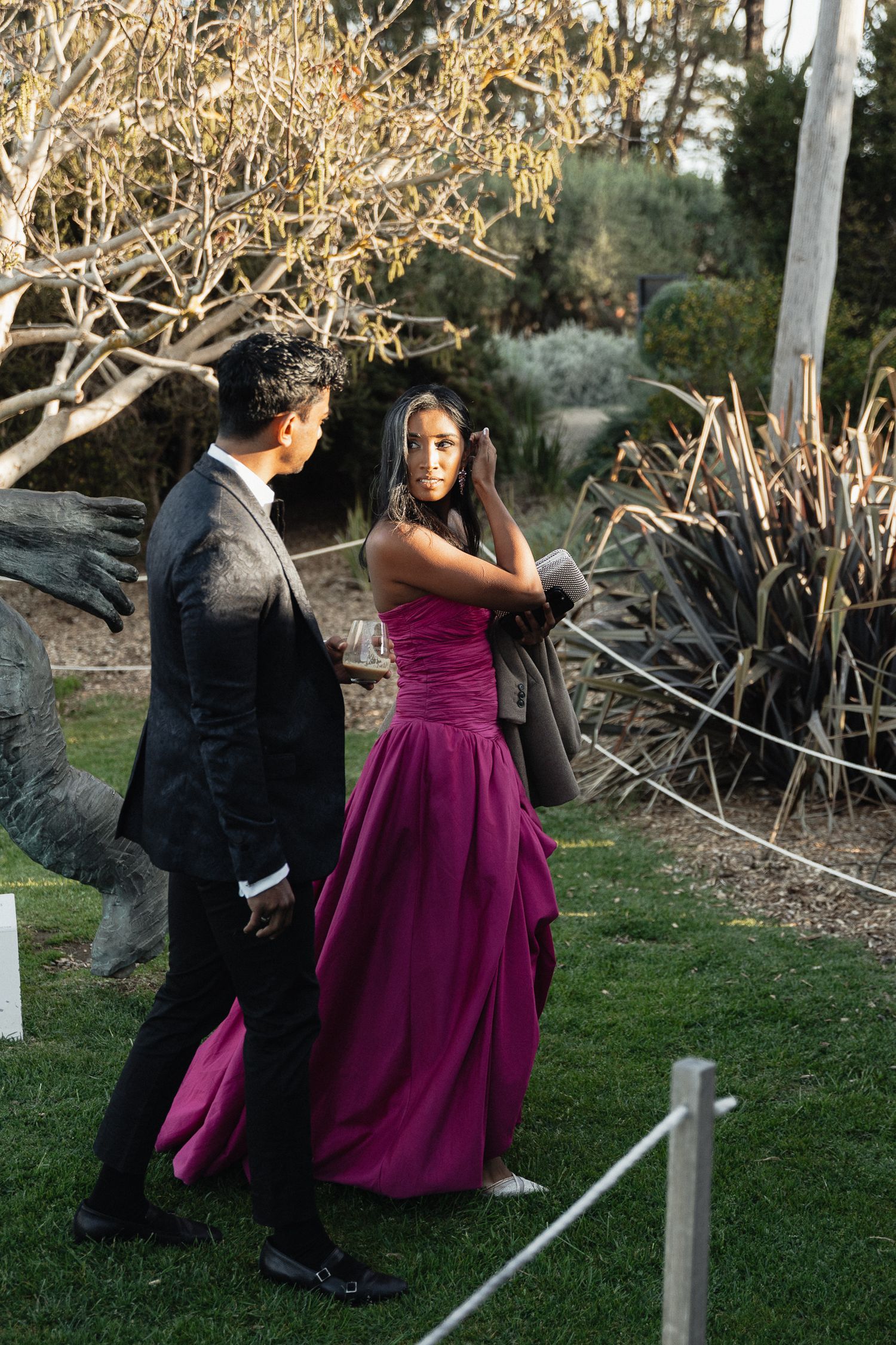 A couple in formal attire embraces during an outdoor photo session in a garden setting.