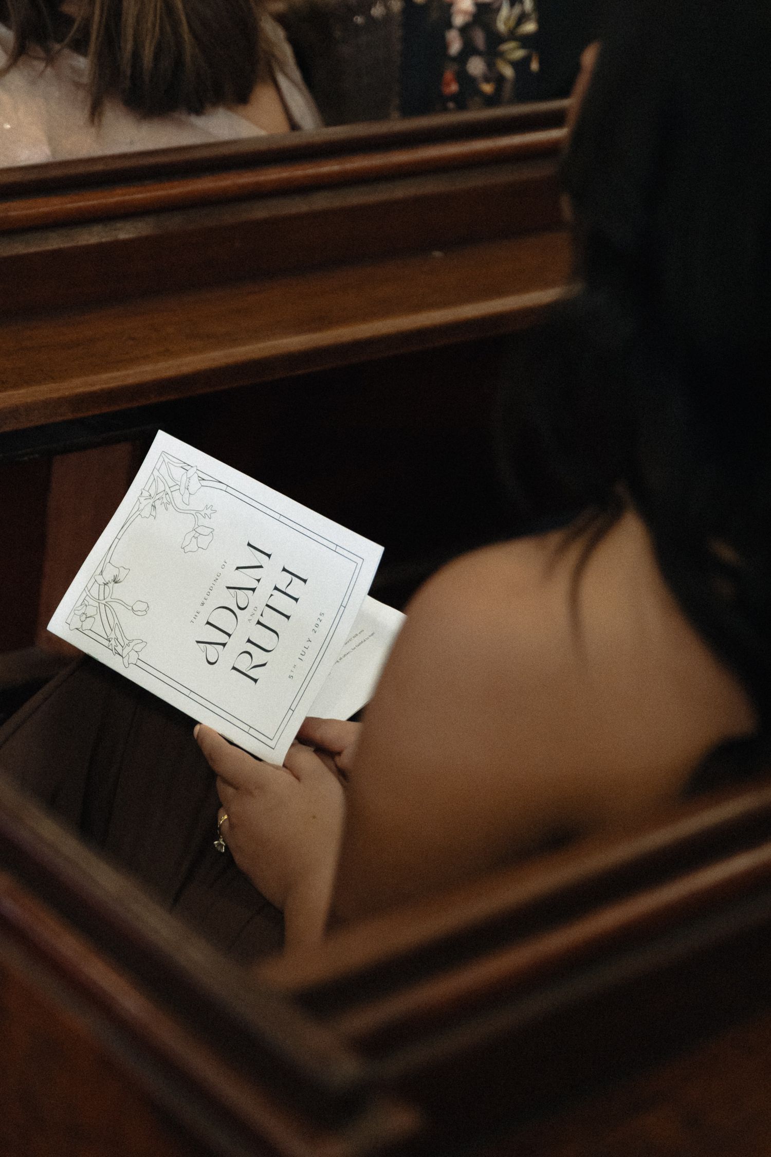 Hands hold a daily faith book against dark wooden church pews in moody lighting.