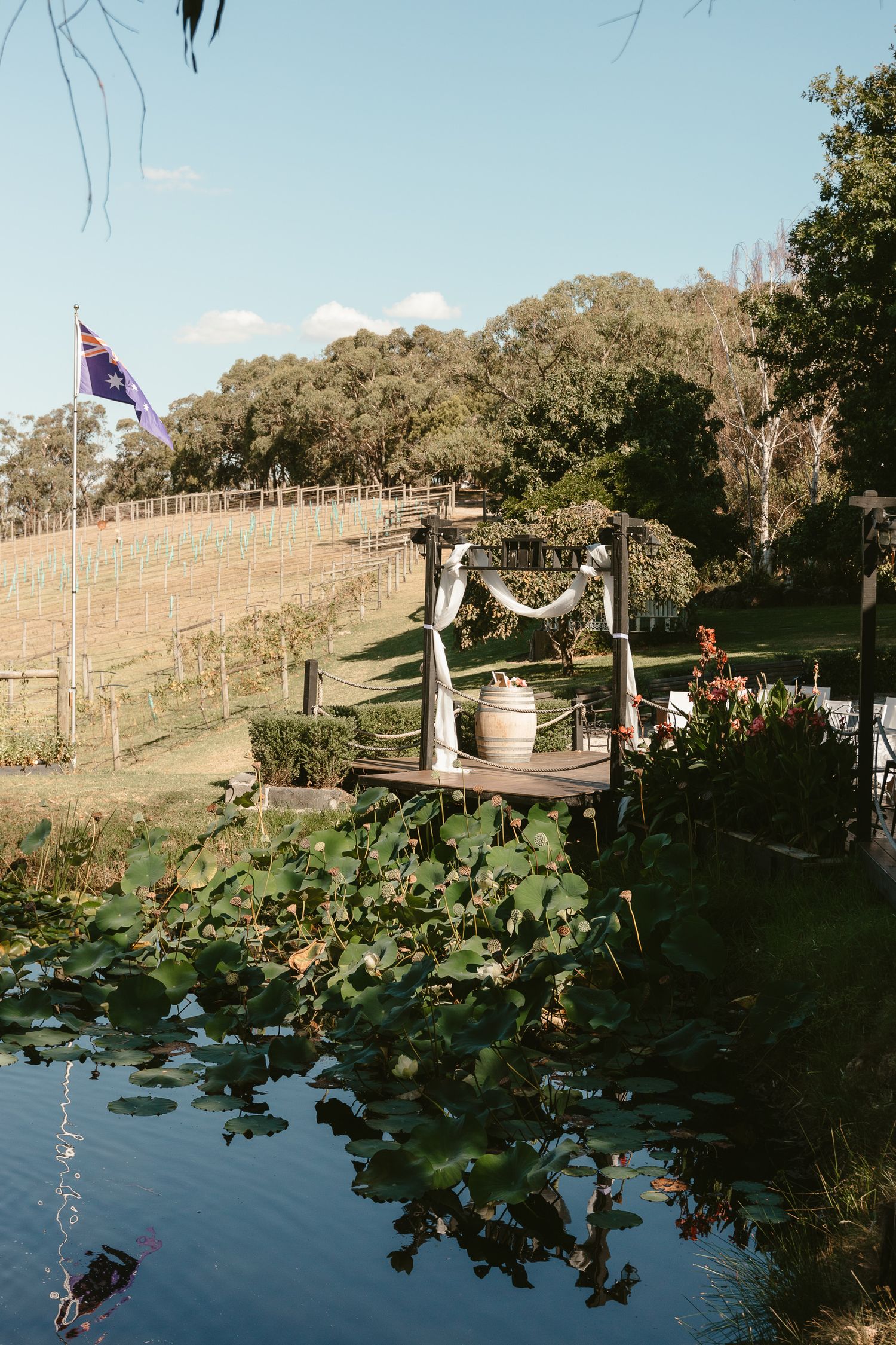 Decorated wooden wedding arch overlooking pond with Australian flag in background.