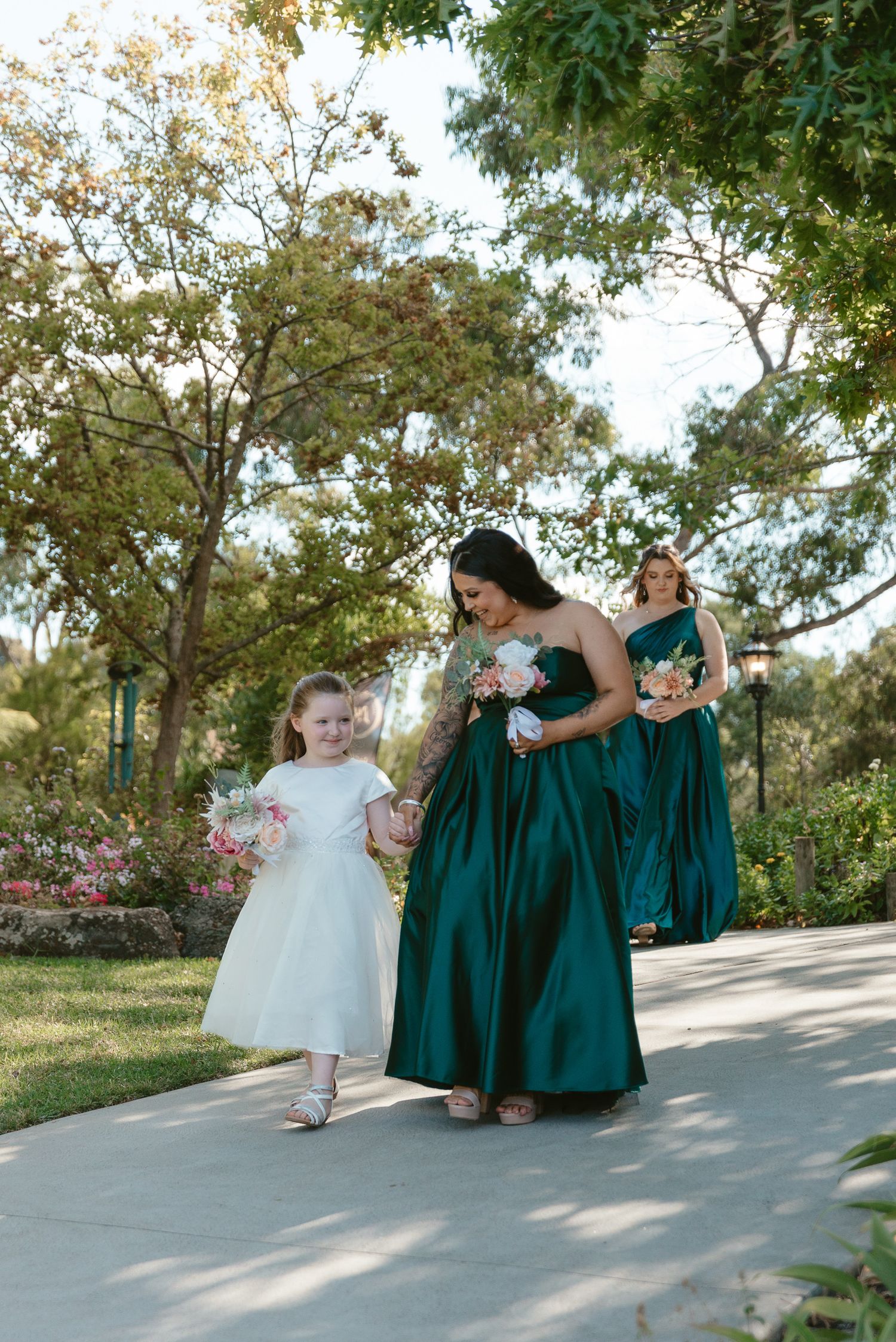 Bridesmaids in emerald green dresses walking with flower girl in white dress.