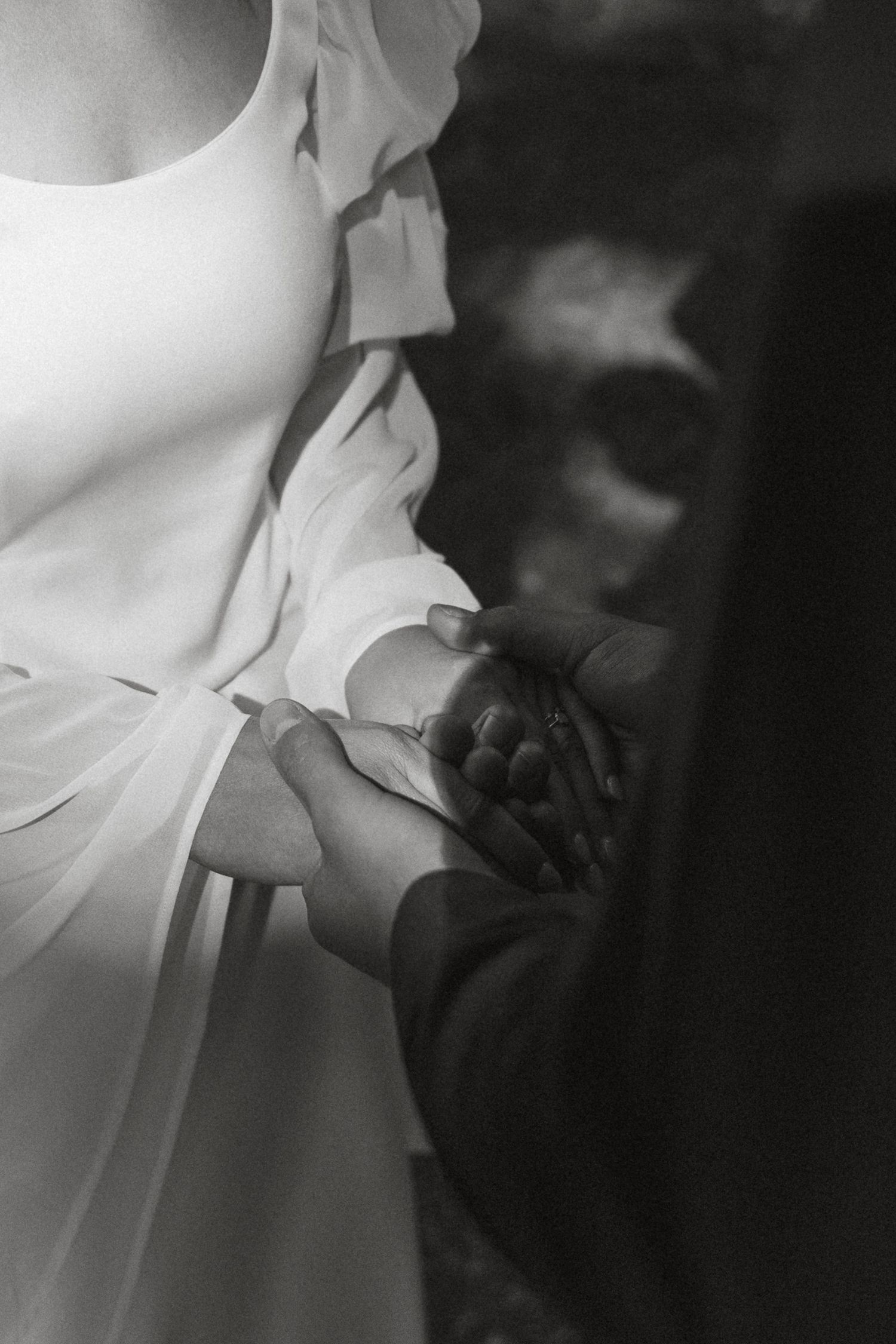 Artful black and white close-up of hands gently holding delicate white fabric in soft natural light.